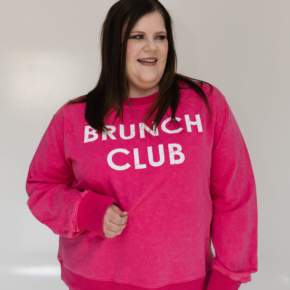 Person wearing a pink 'Brunch Club' sweatshirt against a white background