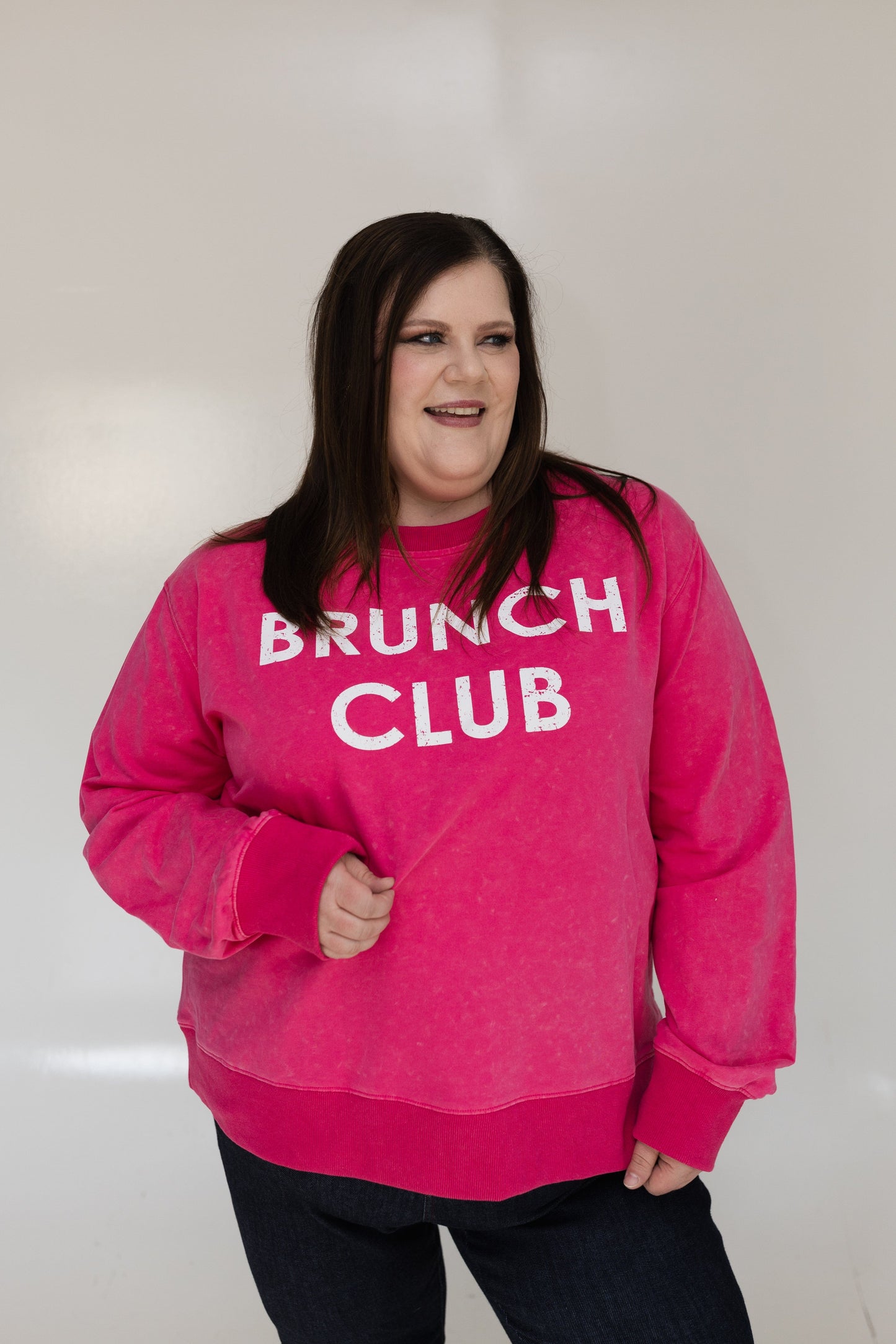 Person wearing a pink 'Brunch Club' sweatshirt against a white background