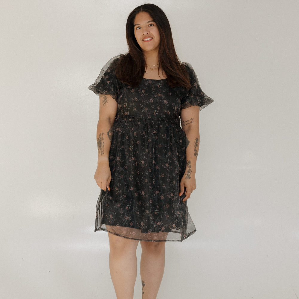 Woman wearing a black floral dress against a plain background
