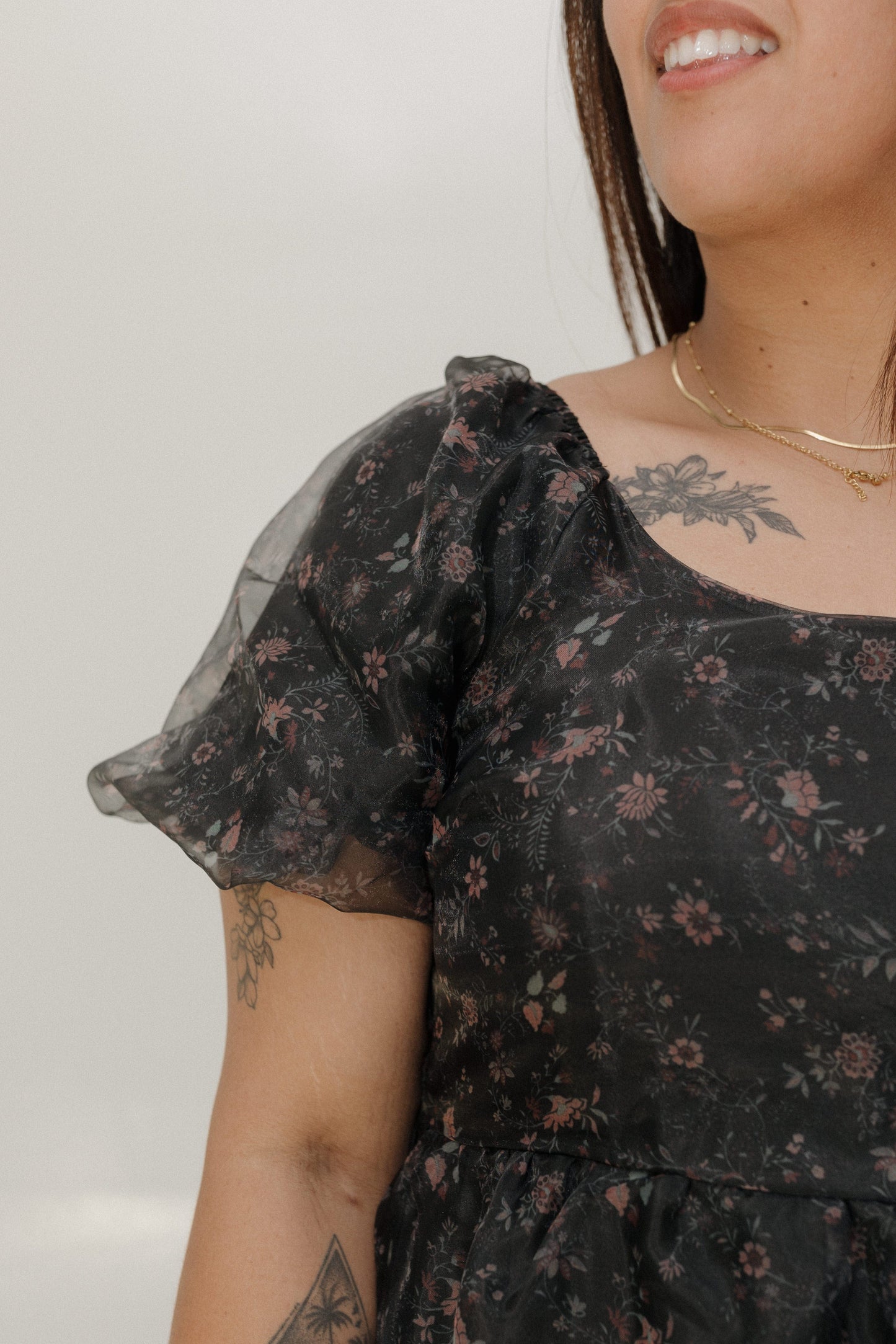Person wearing a black floral dress with sheer sleeves against a plain background