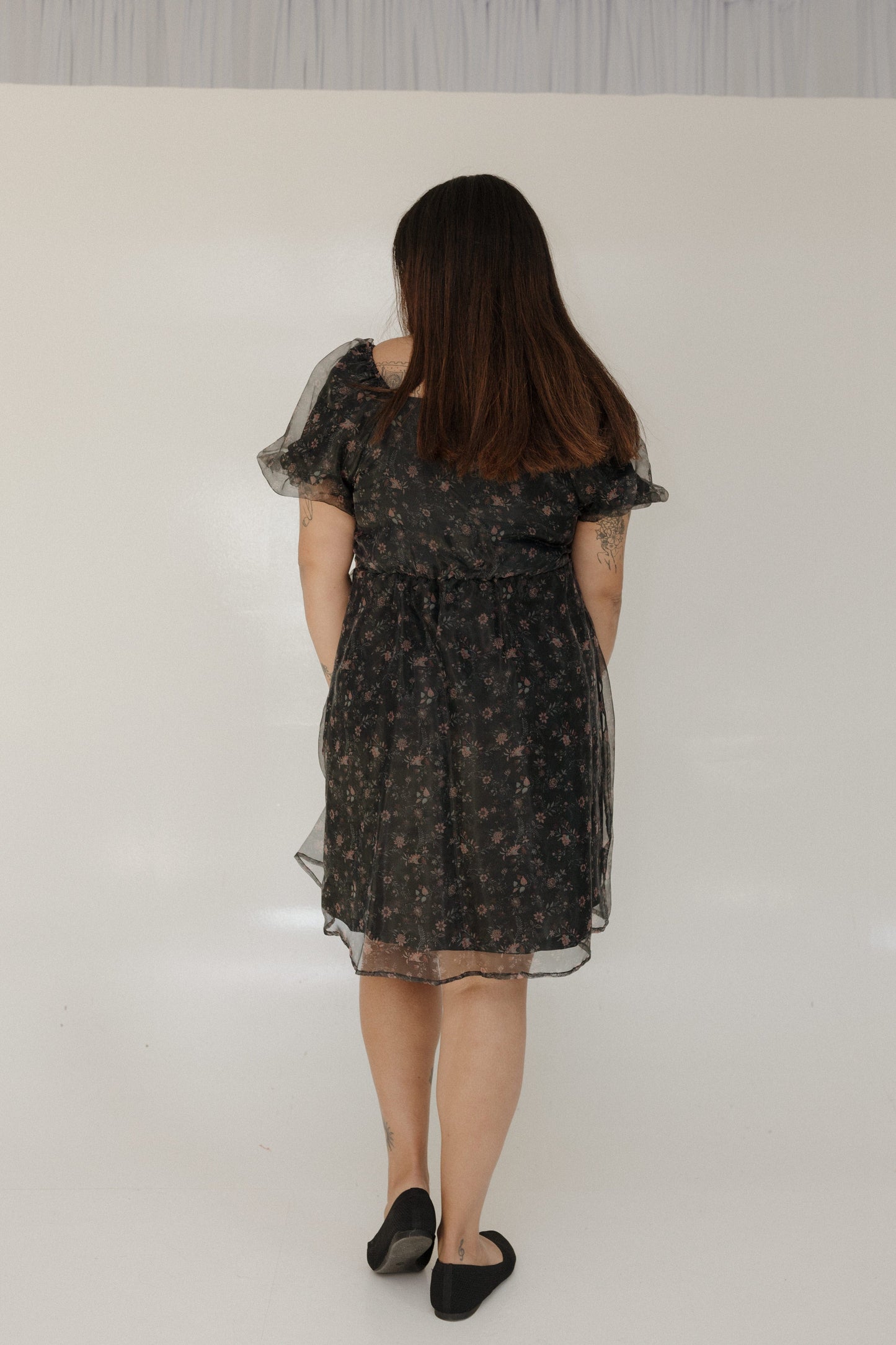 Woman wearing a black floral dress against a plain background
