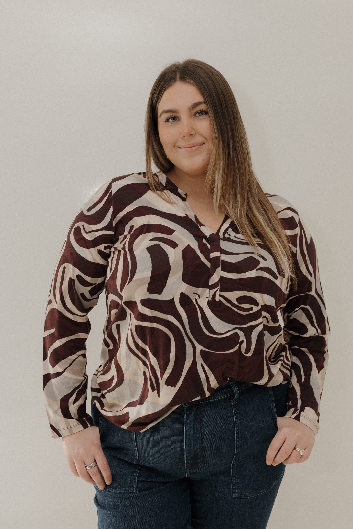 Woman wearing a patterned blouse and jeans against a plain background