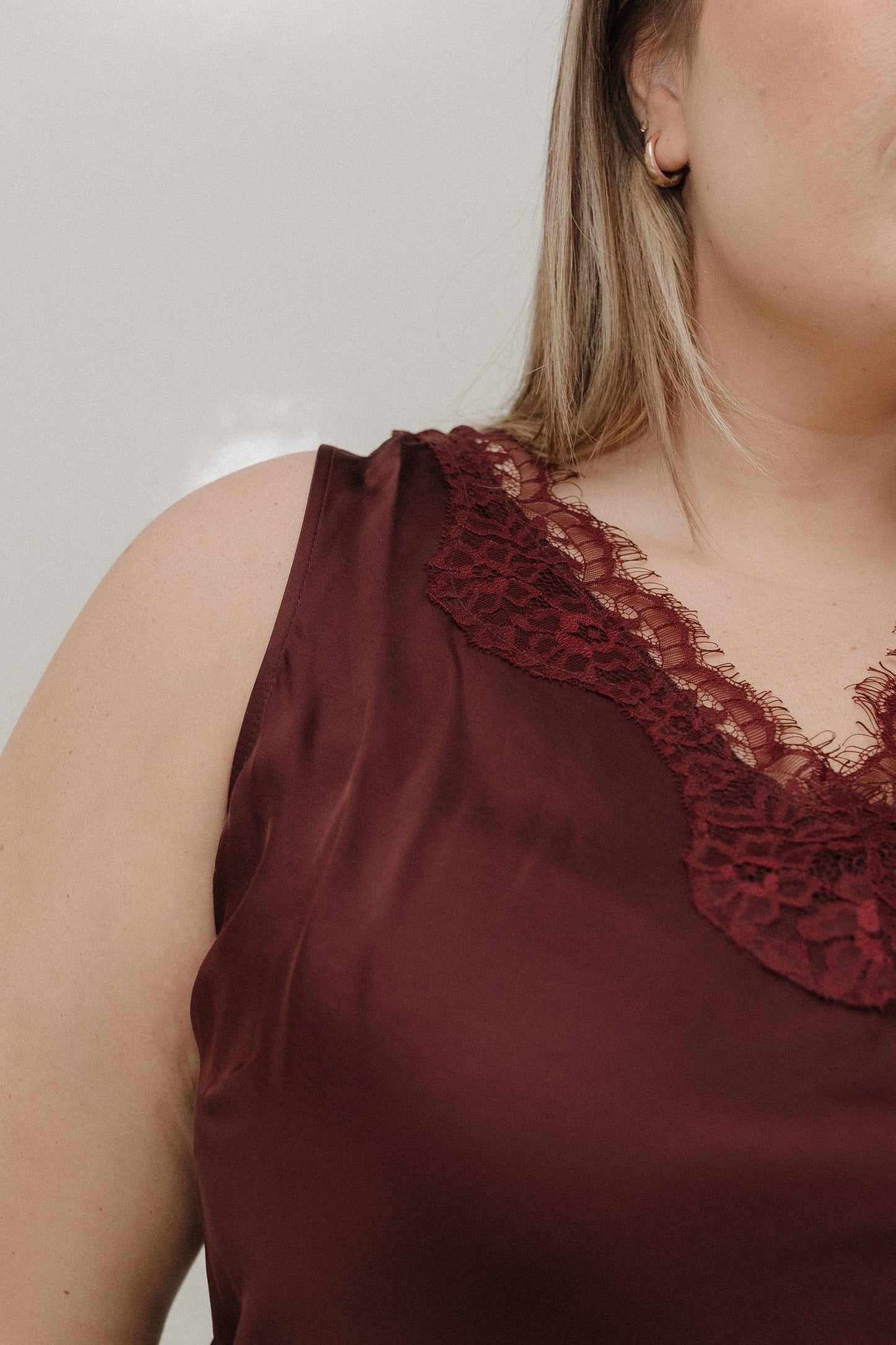 Close-up of a burgundy satin top with lace detailing on a plain background