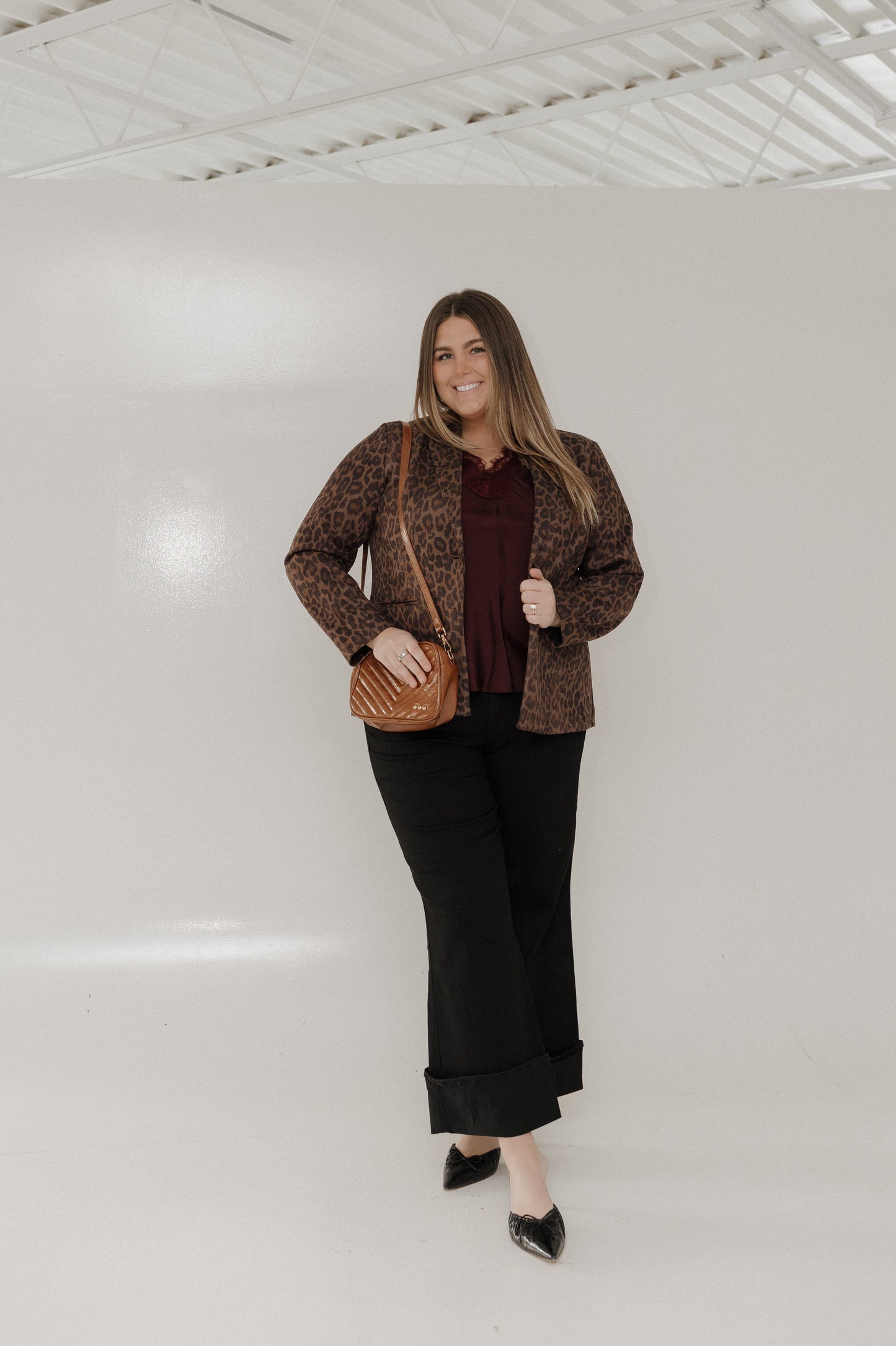 Woman wearing a patterned jacket and black pants against a white wall
