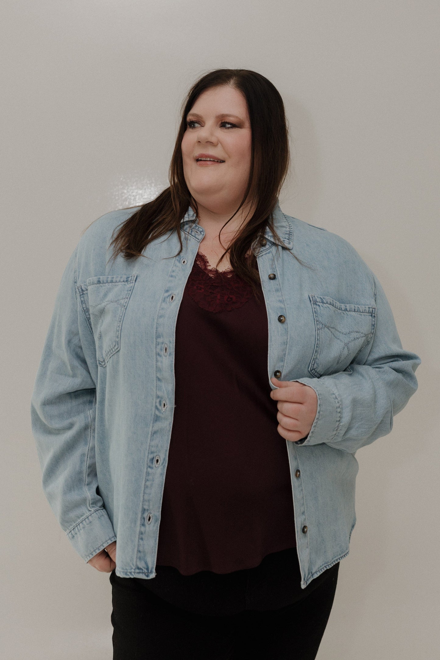 Woman wearing a denim jacket over a dark top against a plain background