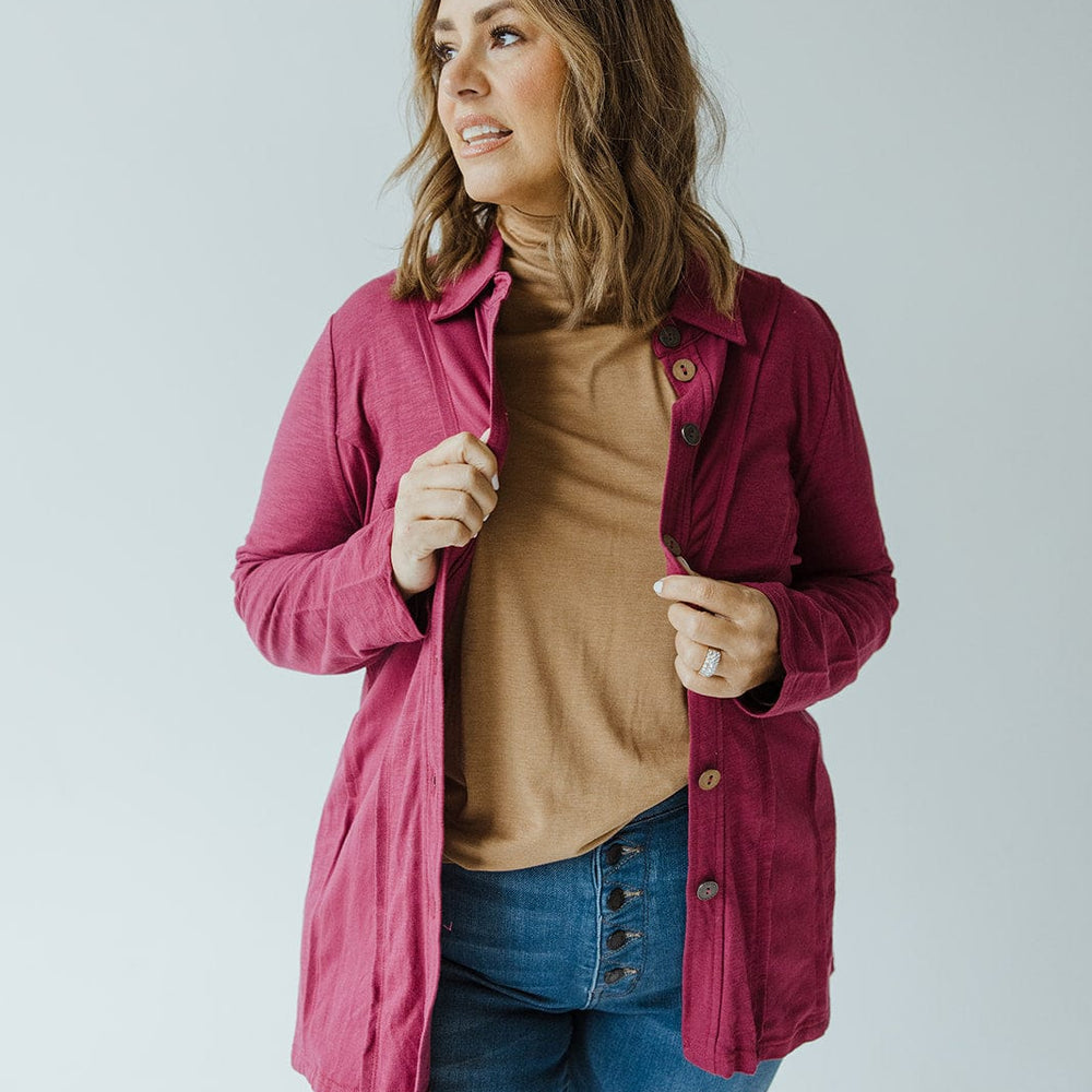 A person with shoulder-length hair wears a pink cardigan over a cranberry button-up blouse with raw seam details from neon buddha, paired with blue jeans. They are facing slightly to the side, adjusting the cardigan with one hand.