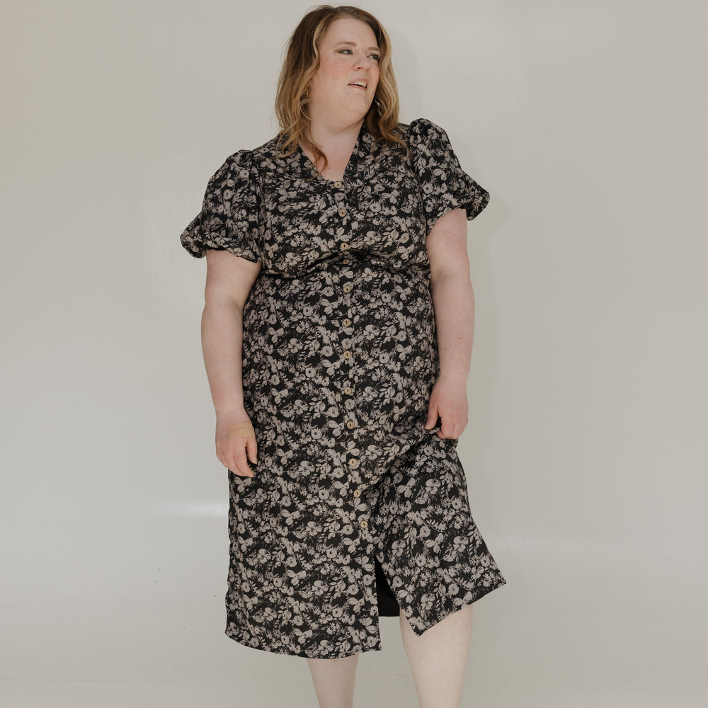 Woman wearing a floral dress standing against a plain white background
