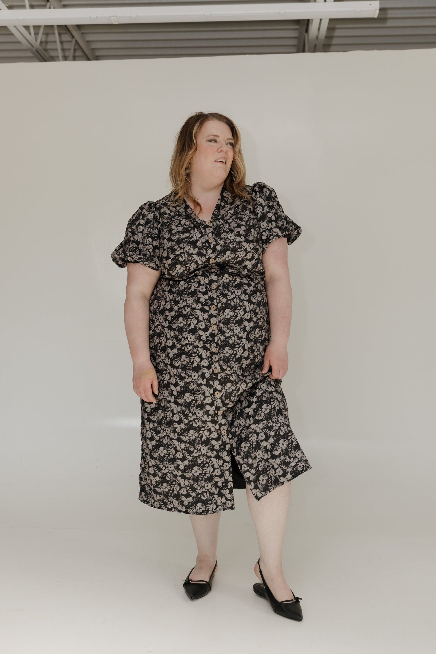 Woman wearing a floral dress standing against a plain white background