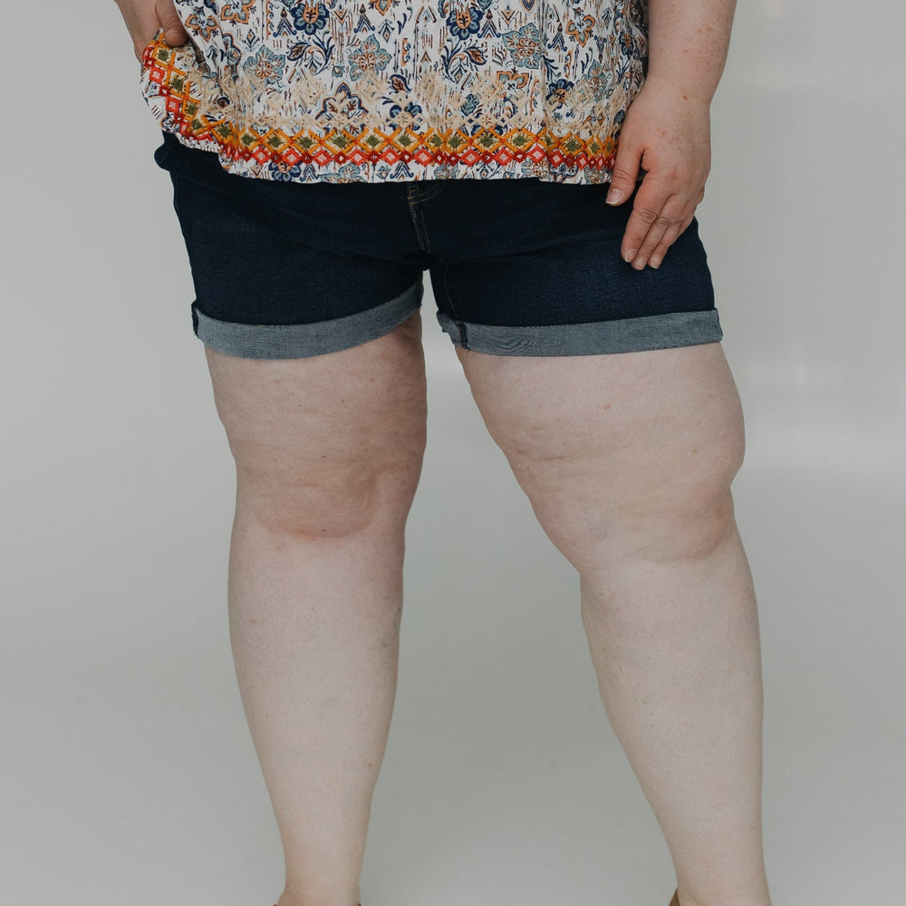 Woman wearing a floral top and denim shorts on a white background