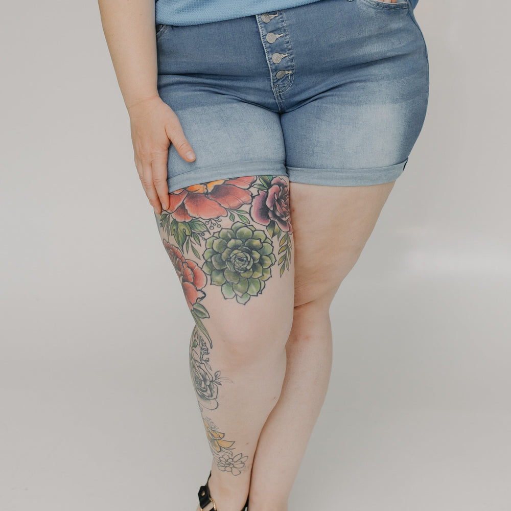 Person wearing blue shorts with floral tattoos on a plain background