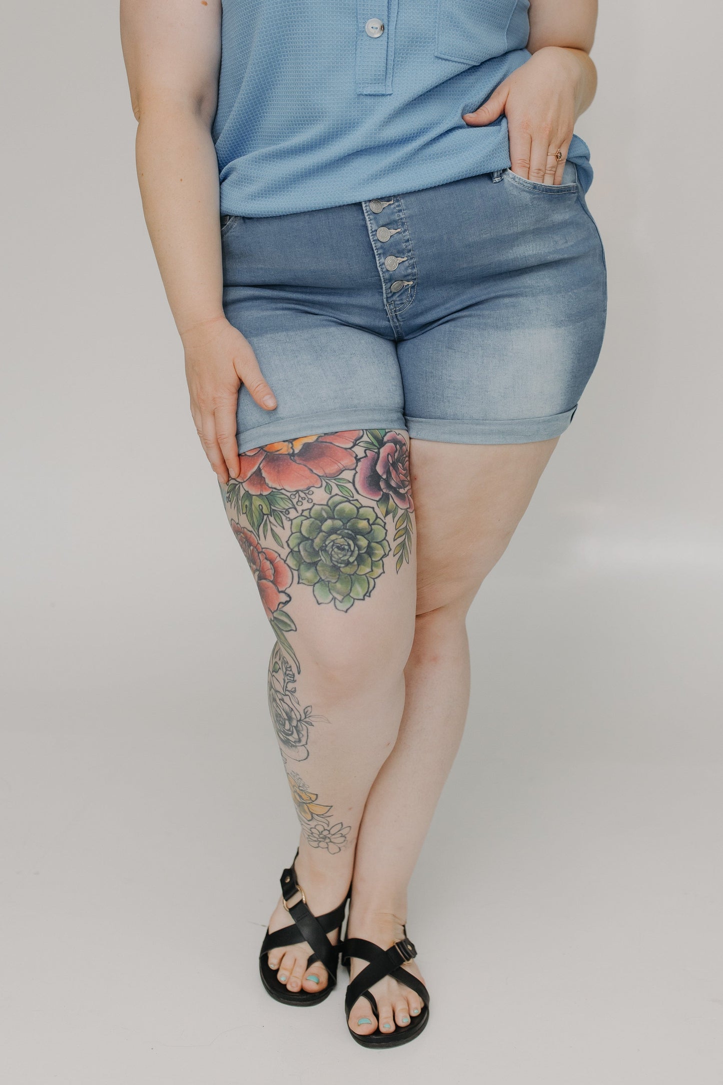 Person wearing blue shorts with floral tattoos on a plain background