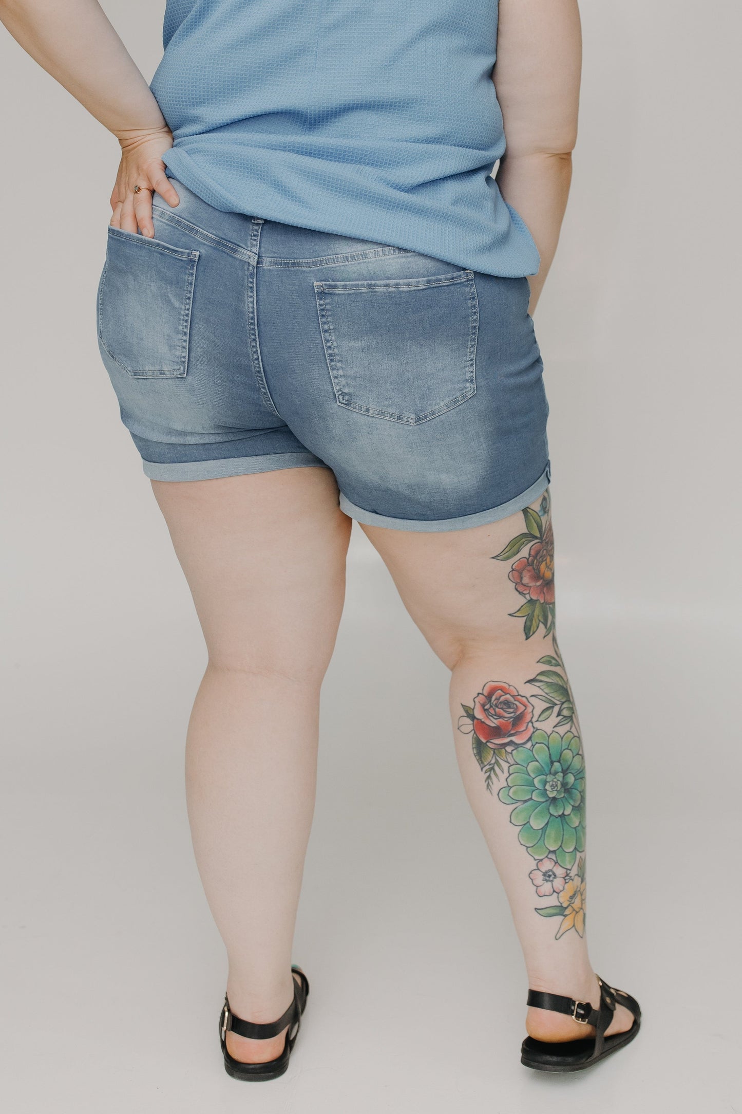 Person wearing denim shorts with a tattoo on a plain background