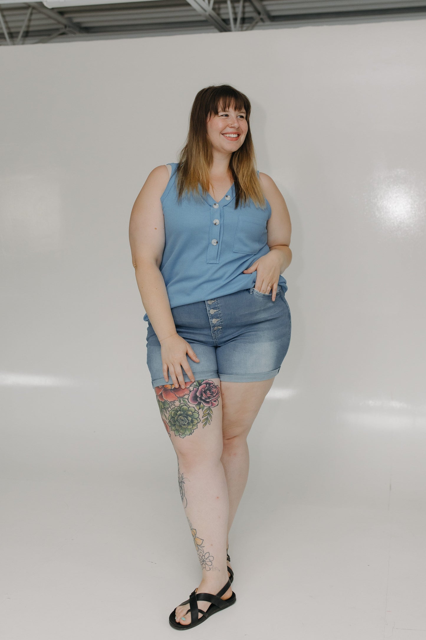Woman wearing a blue sleeveless shirt and denim shorts on a white background