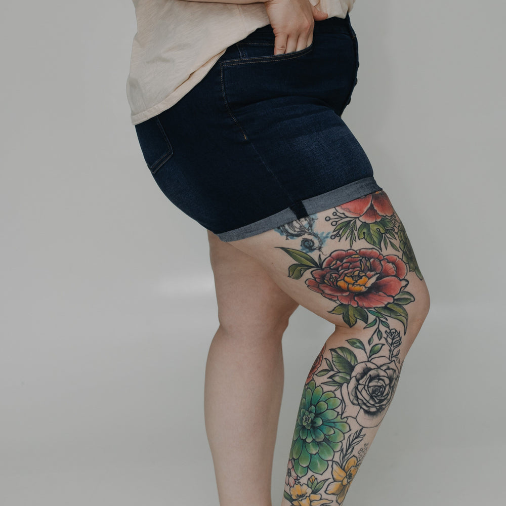 Person wearing dark denim shorts with floral tattoos on a plain background