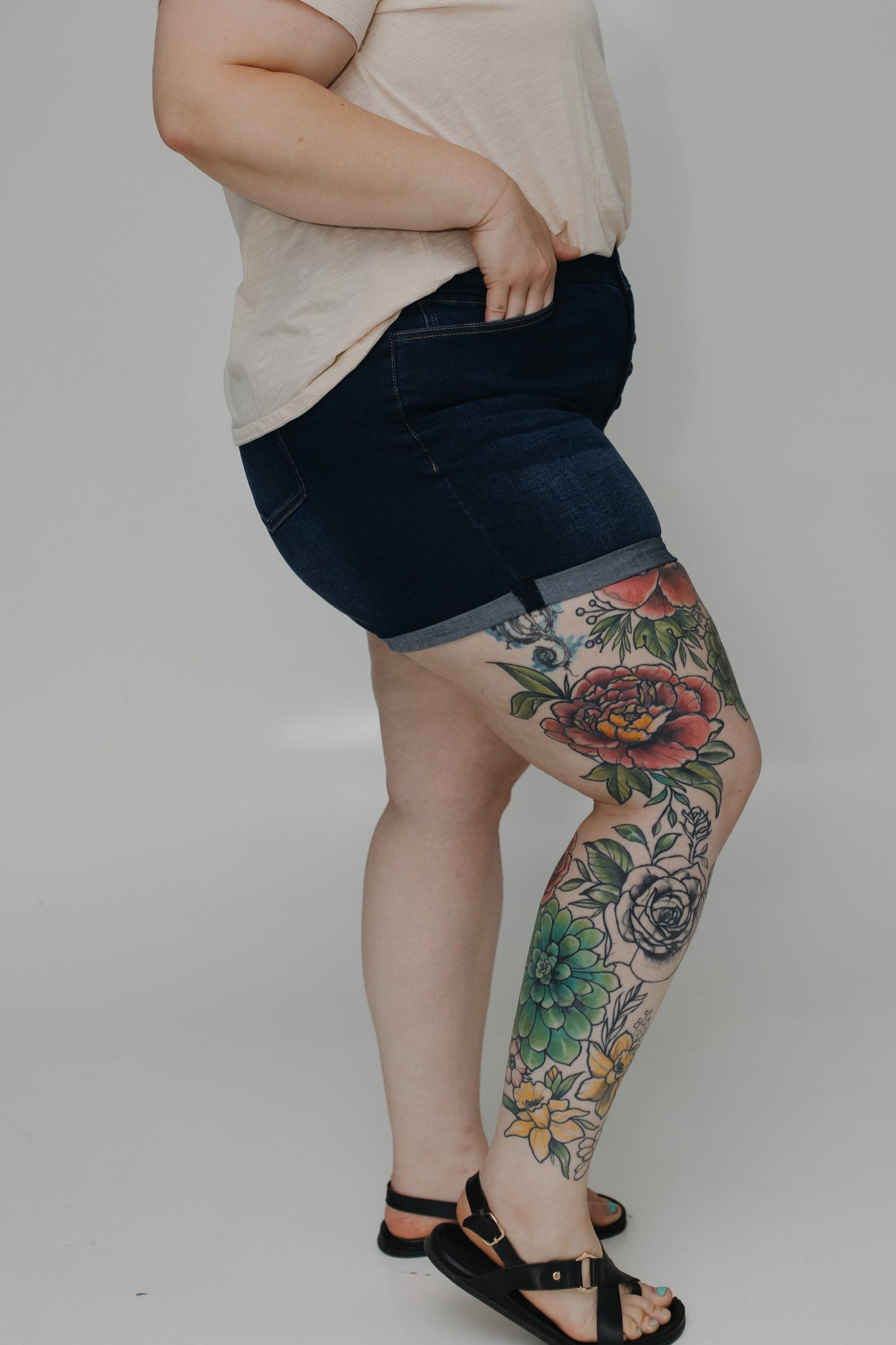 Person wearing dark denim shorts with floral tattoos on a plain background