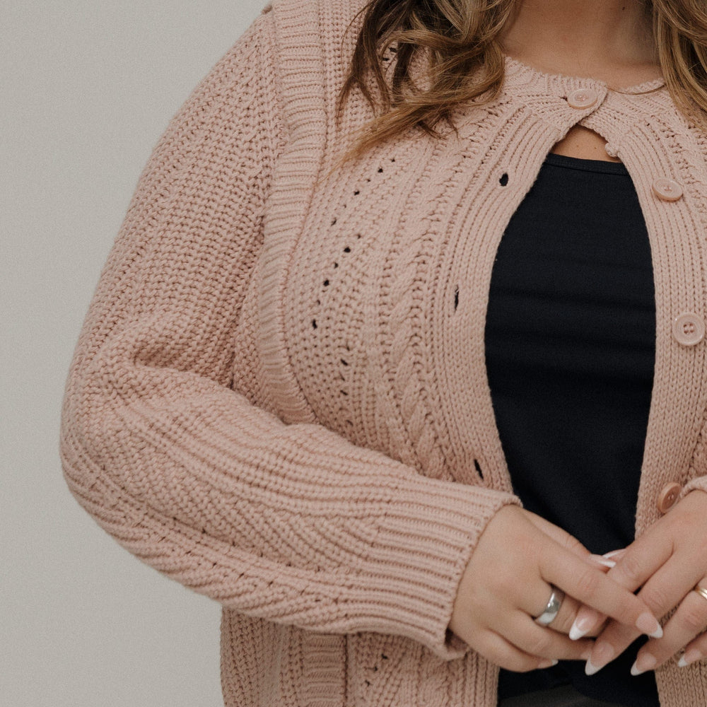 Woman wearing a pink knitted cardigan over a black top against a neutral background