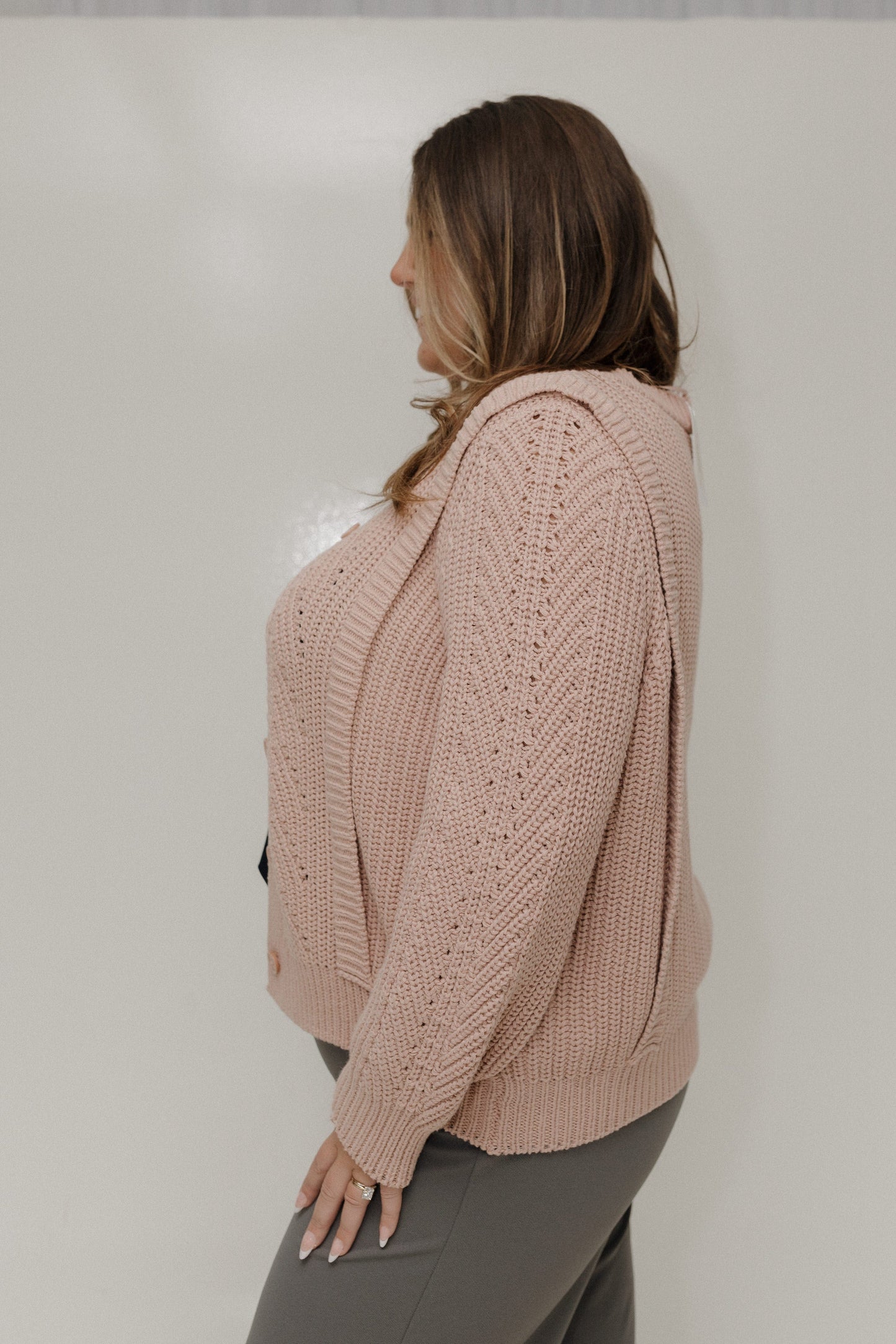 Woman wearing a pink knitted cardigan against a plain background
