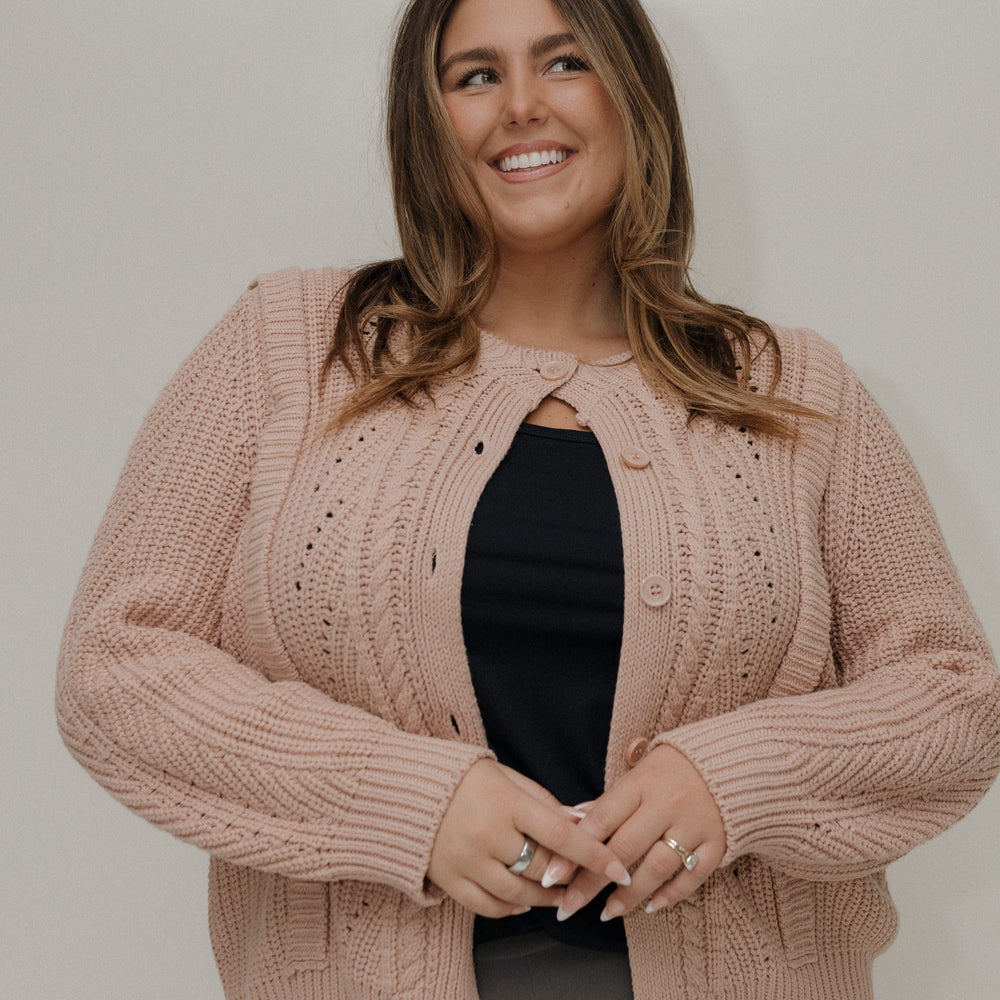 Woman wearing a pink knitted cardigan over a black top against a plain background