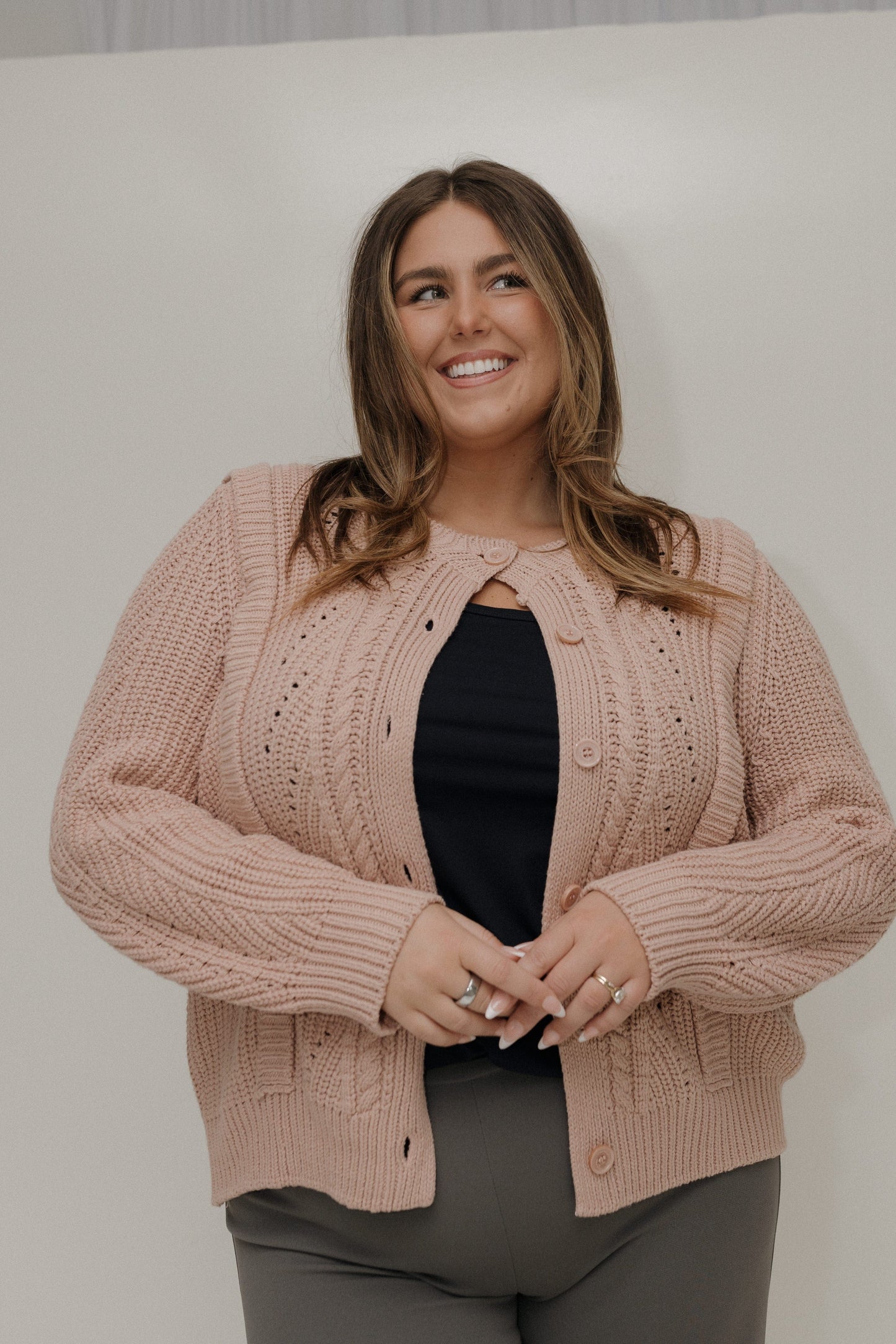 Woman wearing a pink knitted cardigan over a black top against a plain background