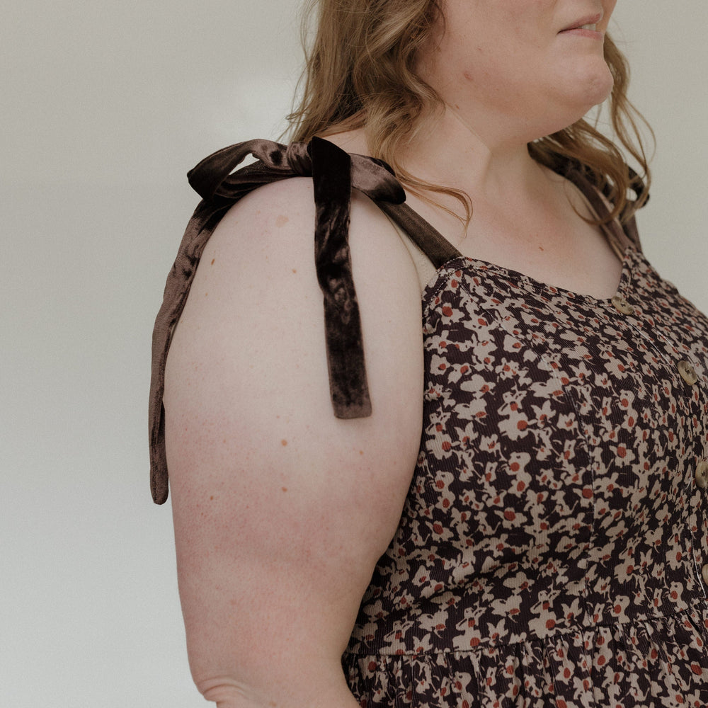Woman wearing a floral dress with leopard print straps against a plain background