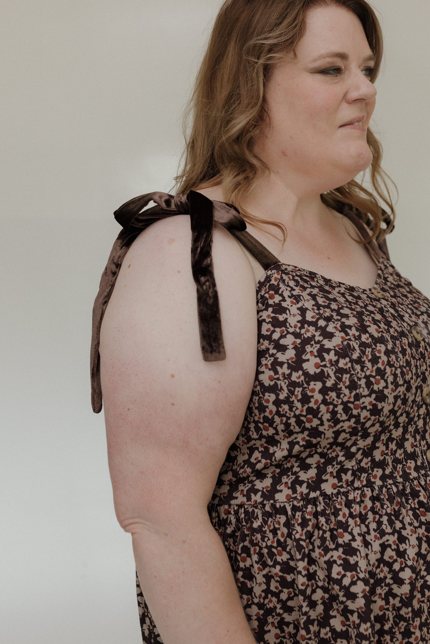 Woman wearing a floral dress with leopard print straps against a plain background