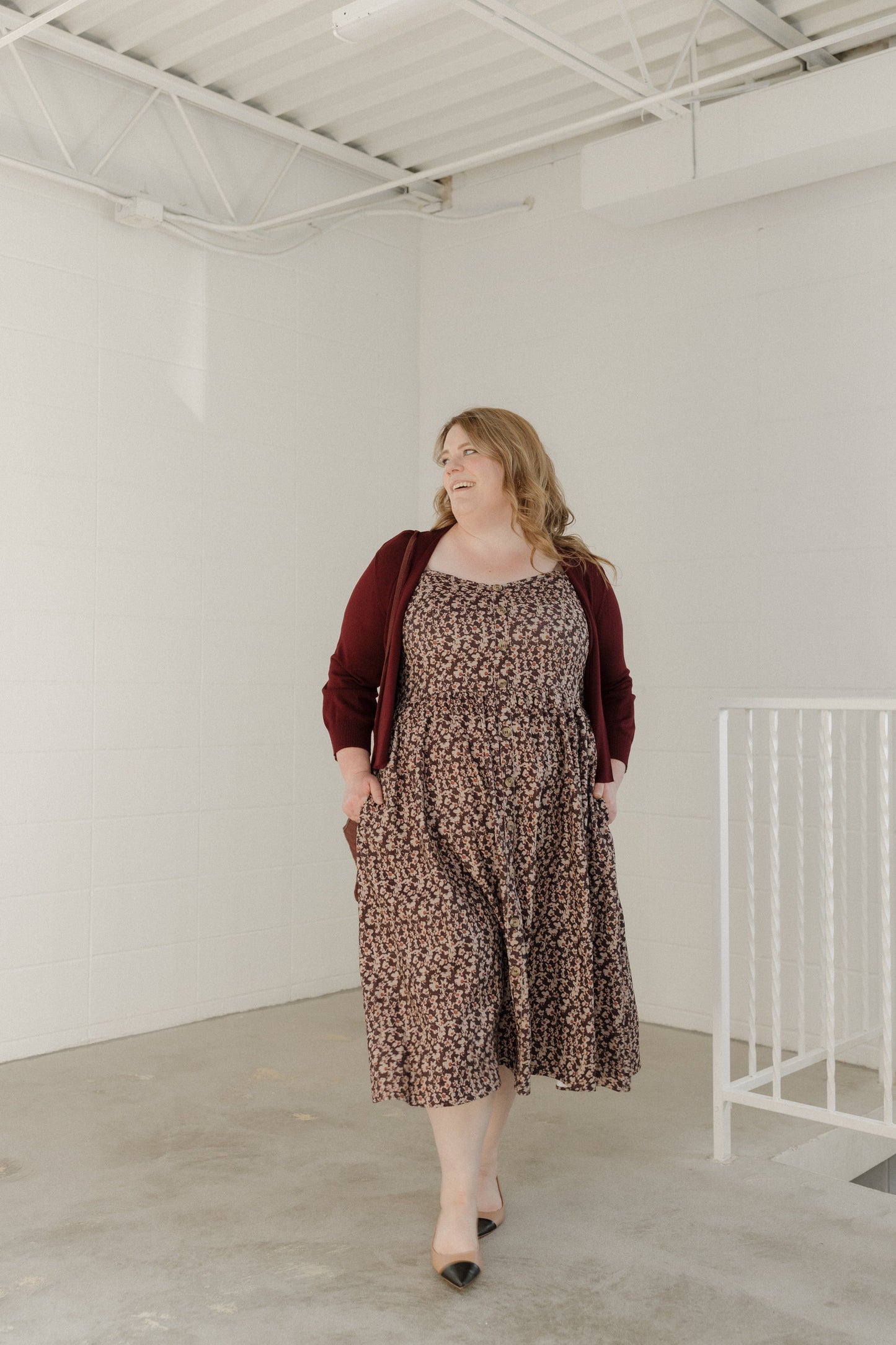 Woman wearing a patterned dress and red cardigan in a minimalistic room.