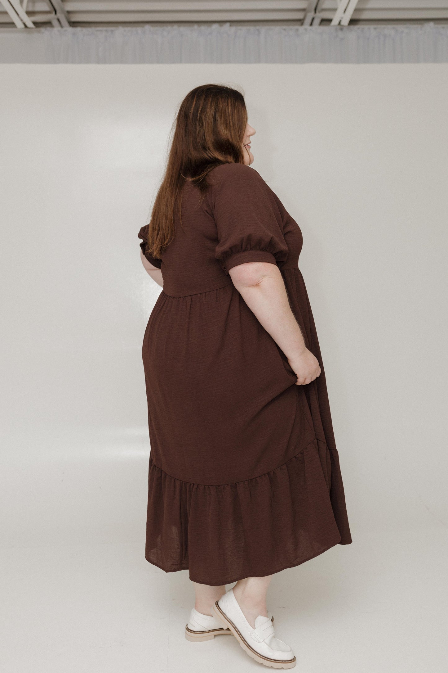 Person wearing a brown dress standing against a white wall