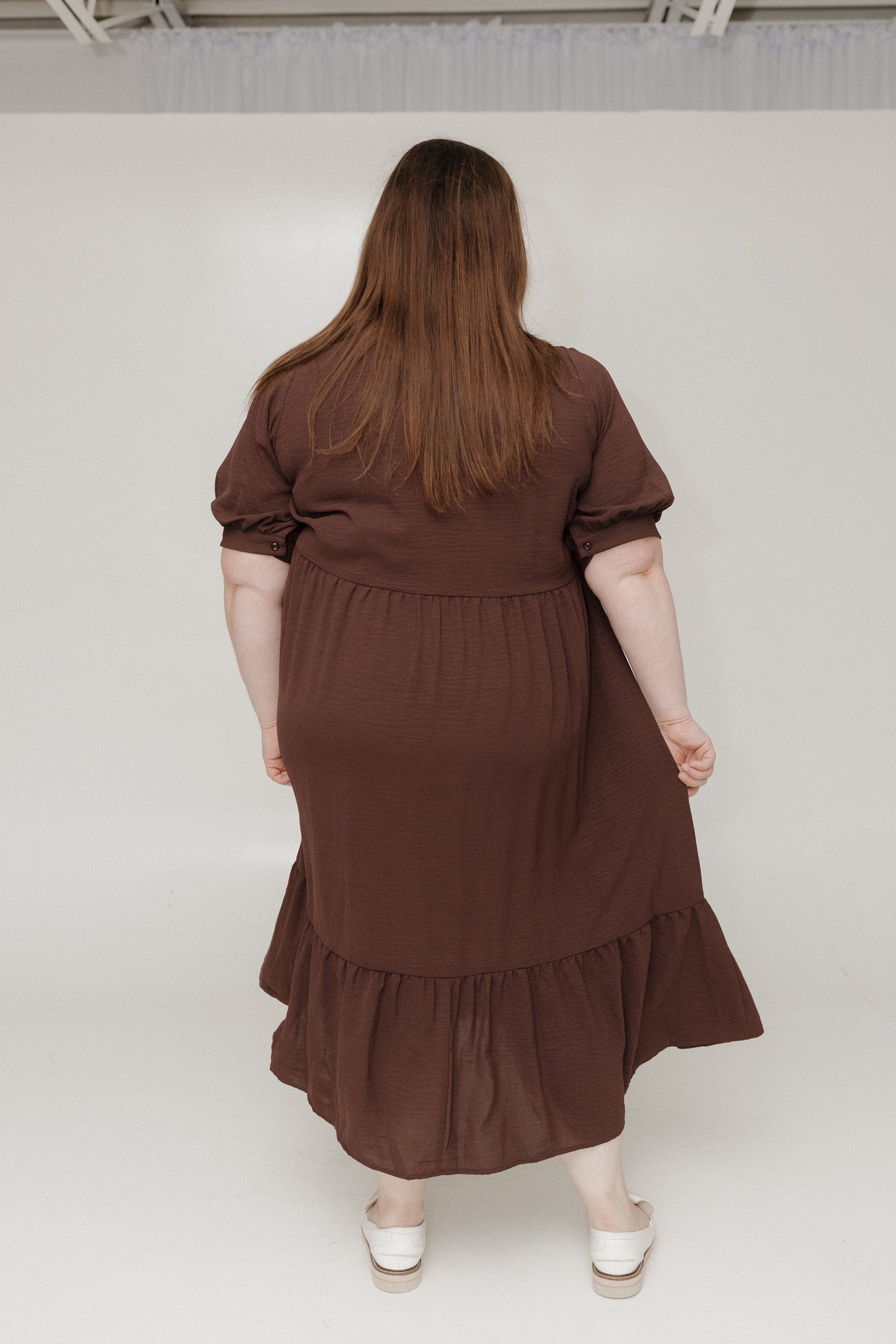 Person wearing a brown dress with ruffled layers on a white background