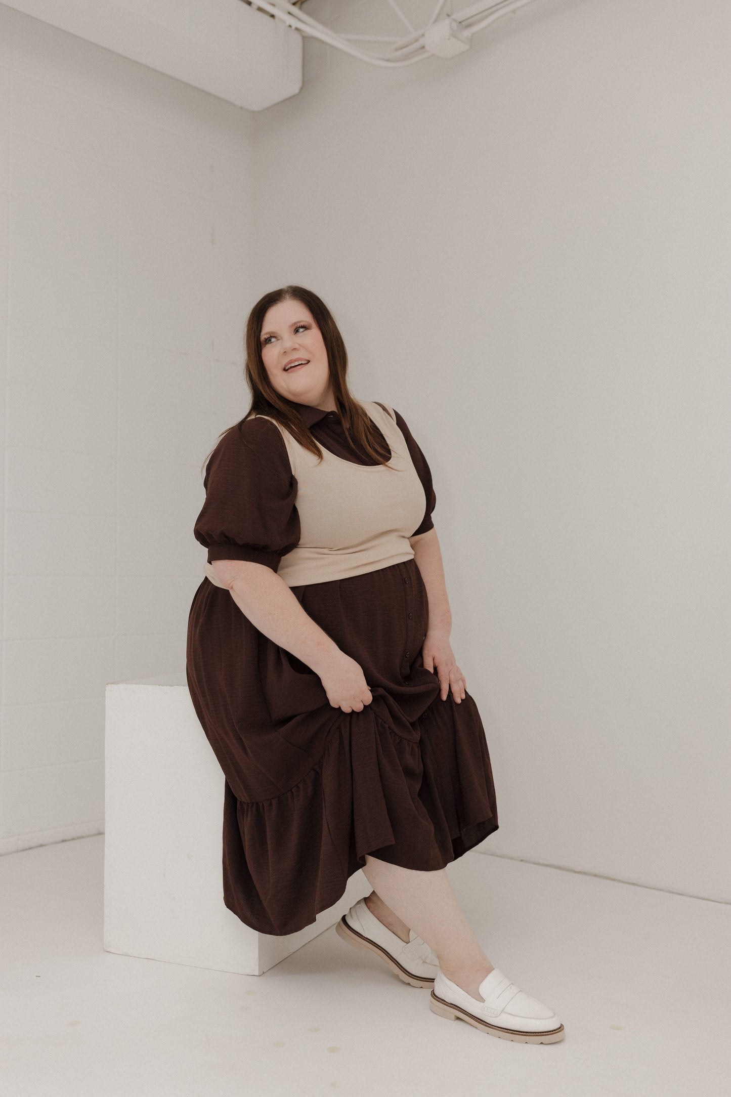 Woman wearing a brown dress with a beige top in a minimal white room