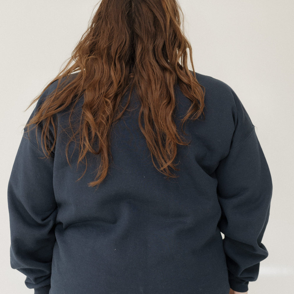 Person wearing a dark blue sweatshirt and light blue jeans against a white background