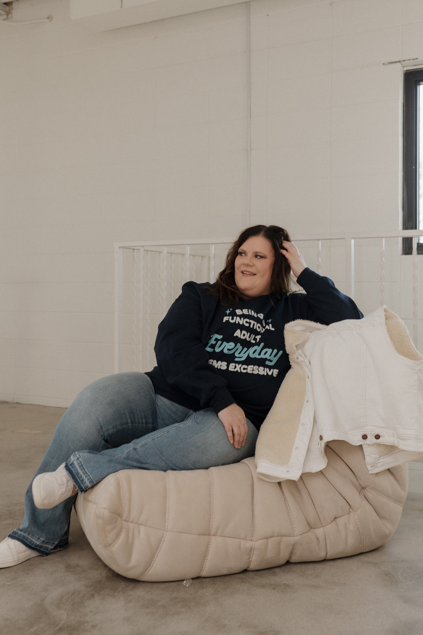 Person sitting on a bean bag chair wearing a black sweatshirt with text and jeans.
