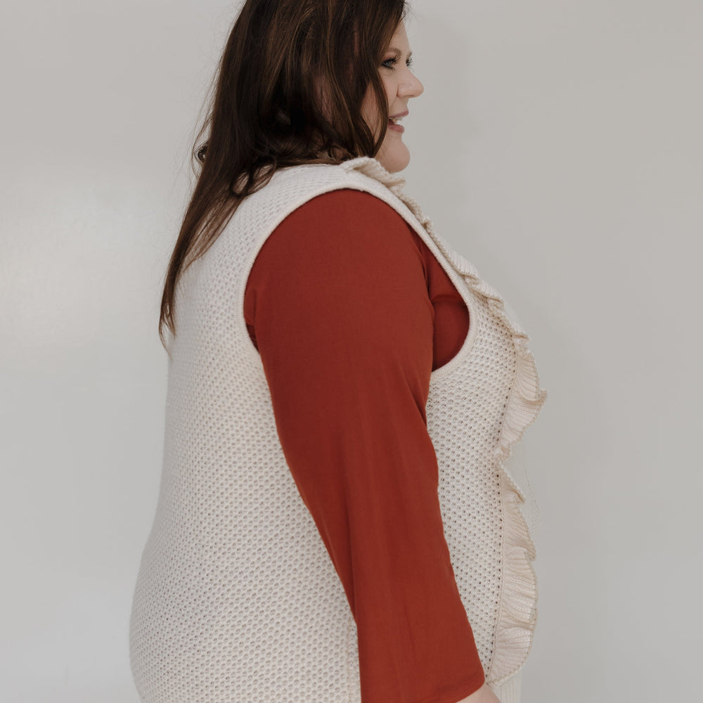 Woman wearing a beige vest over a red shirt with a plain background