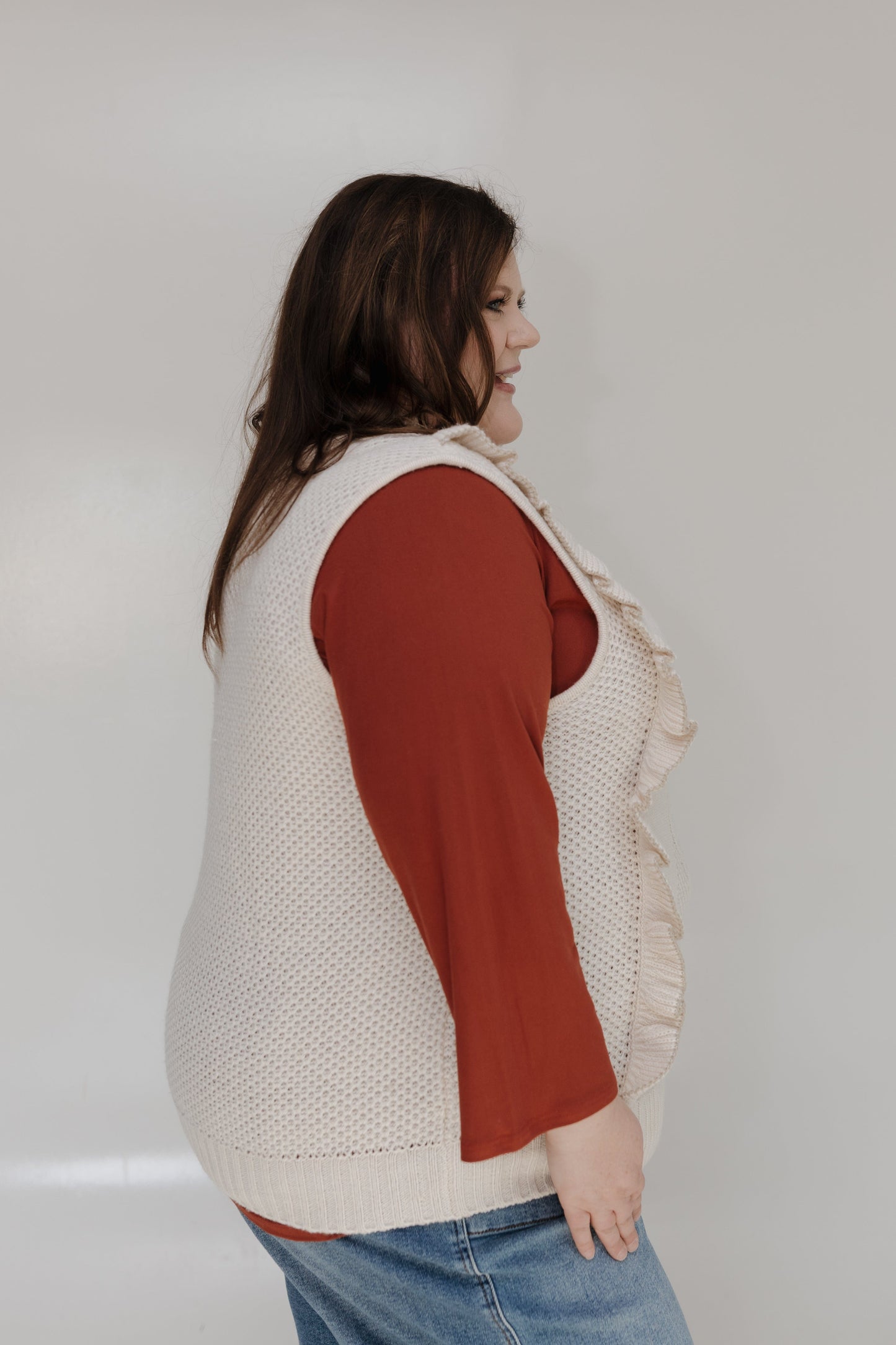 Woman wearing a beige vest over a red shirt with a plain background