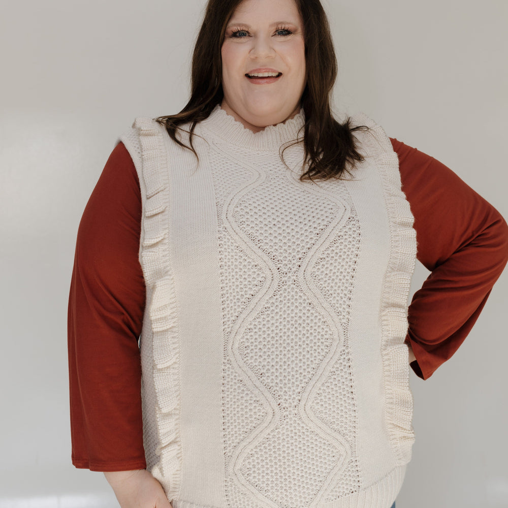 Person wearing a cream knitted vest over a red shirt with a plain background