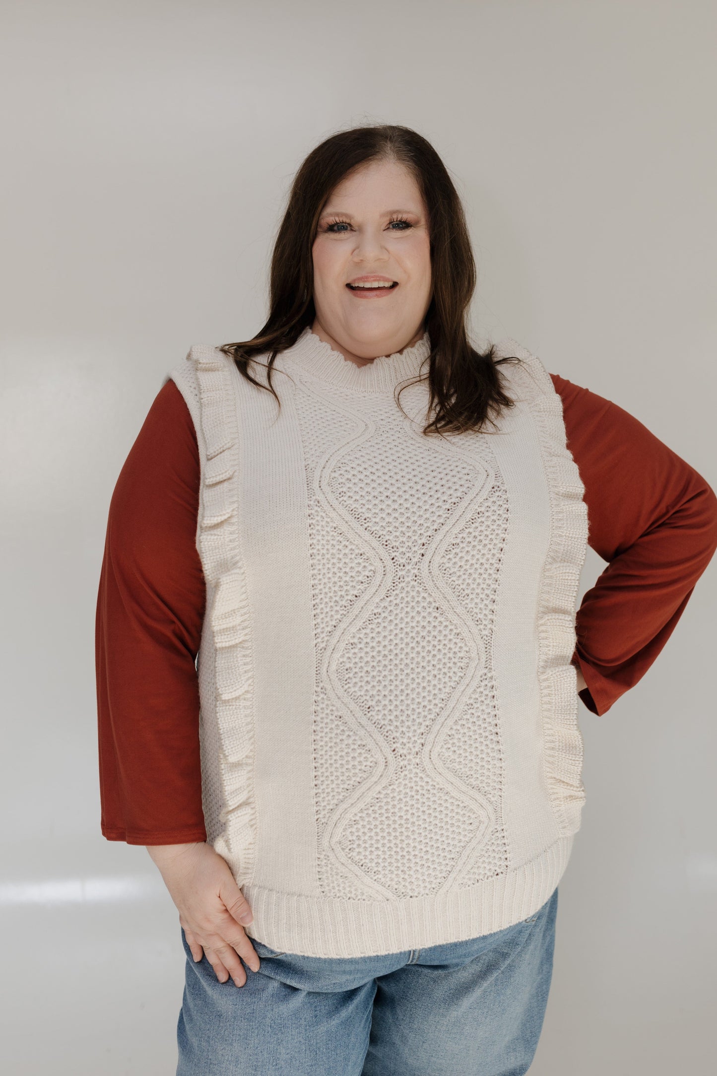 Person wearing a cream knitted vest over a red shirt with a plain background