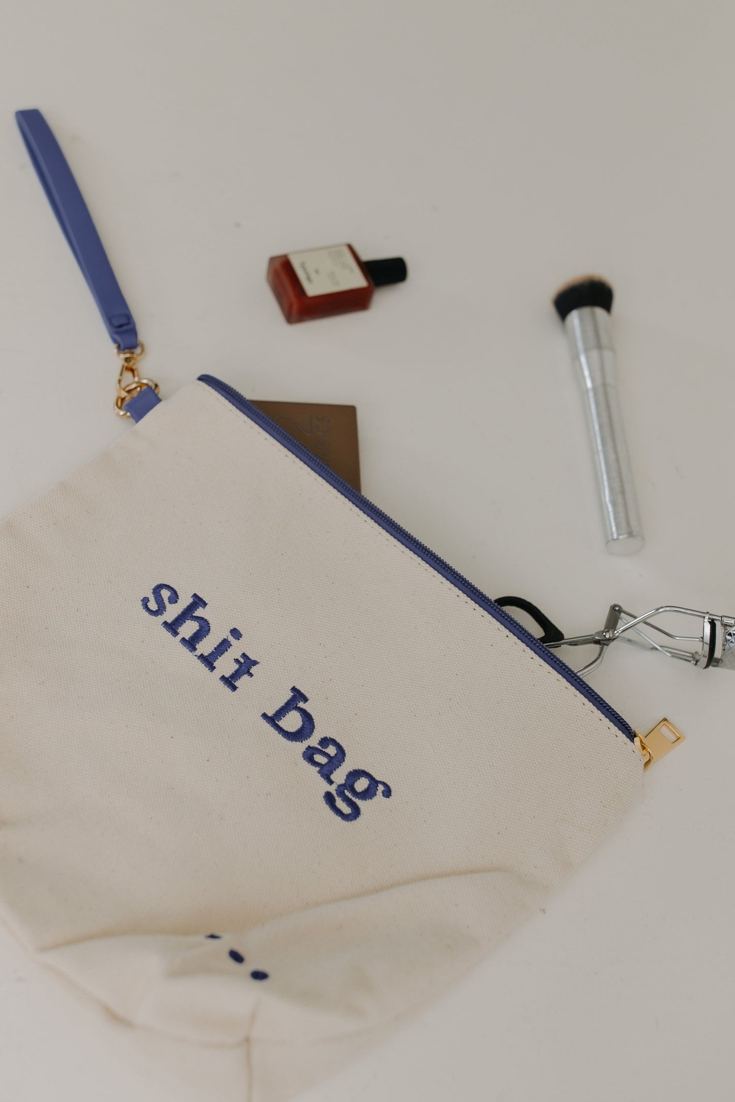 Beige pouch with 'shit Bag' text on a white background with makeup items.