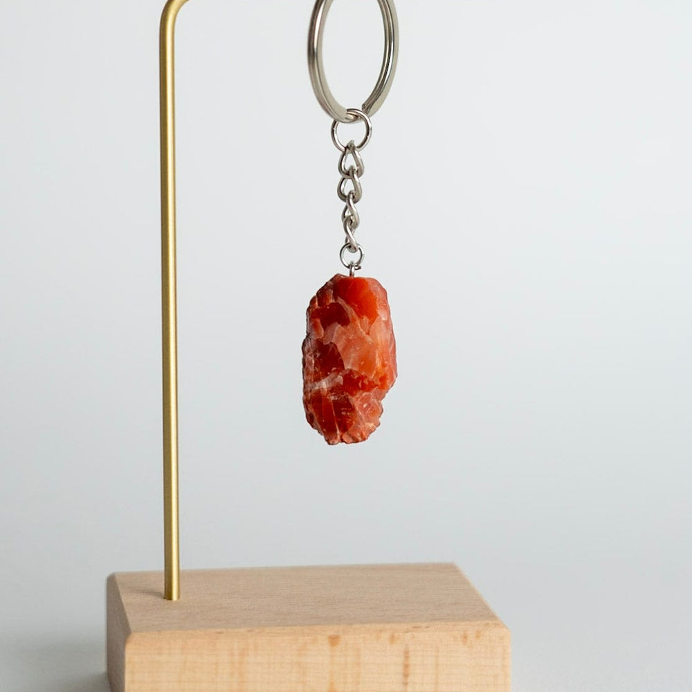 Keychain with a Carnelian stone pendant on a brass stand with a wooden base against a light gray background