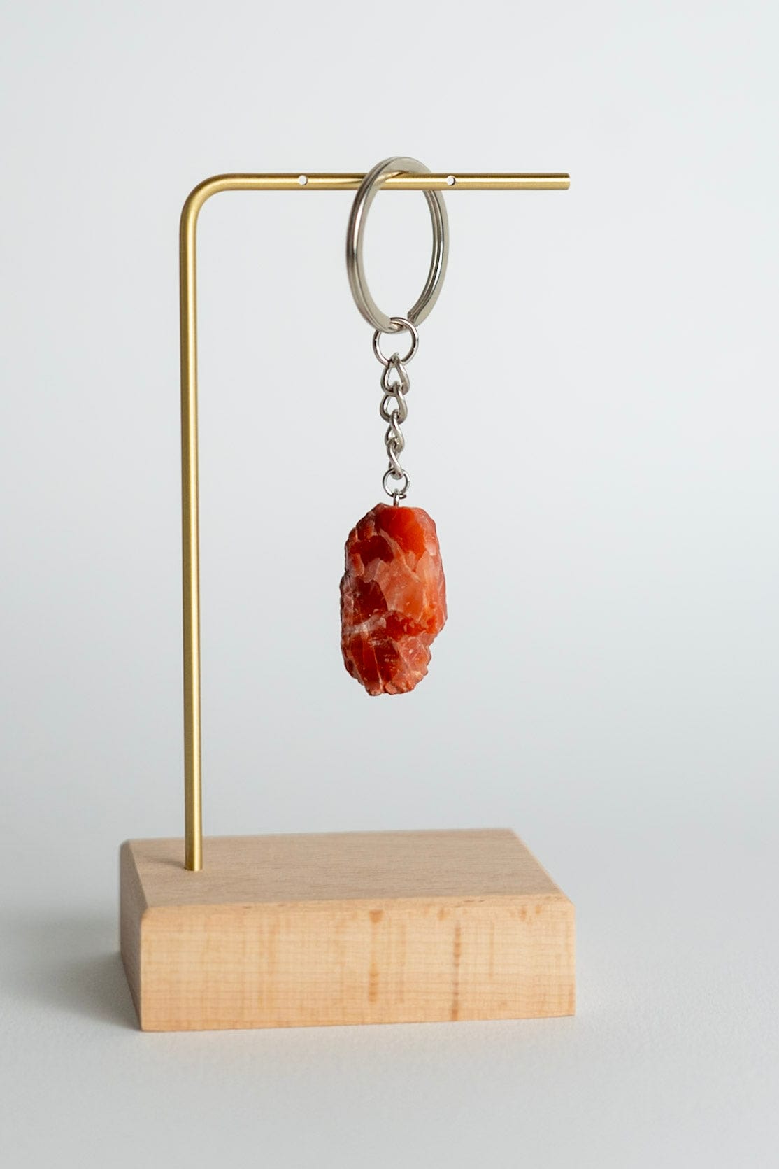 Keychain with a Carnelian stone pendant on a brass stand with a wooden base against a light gray background
