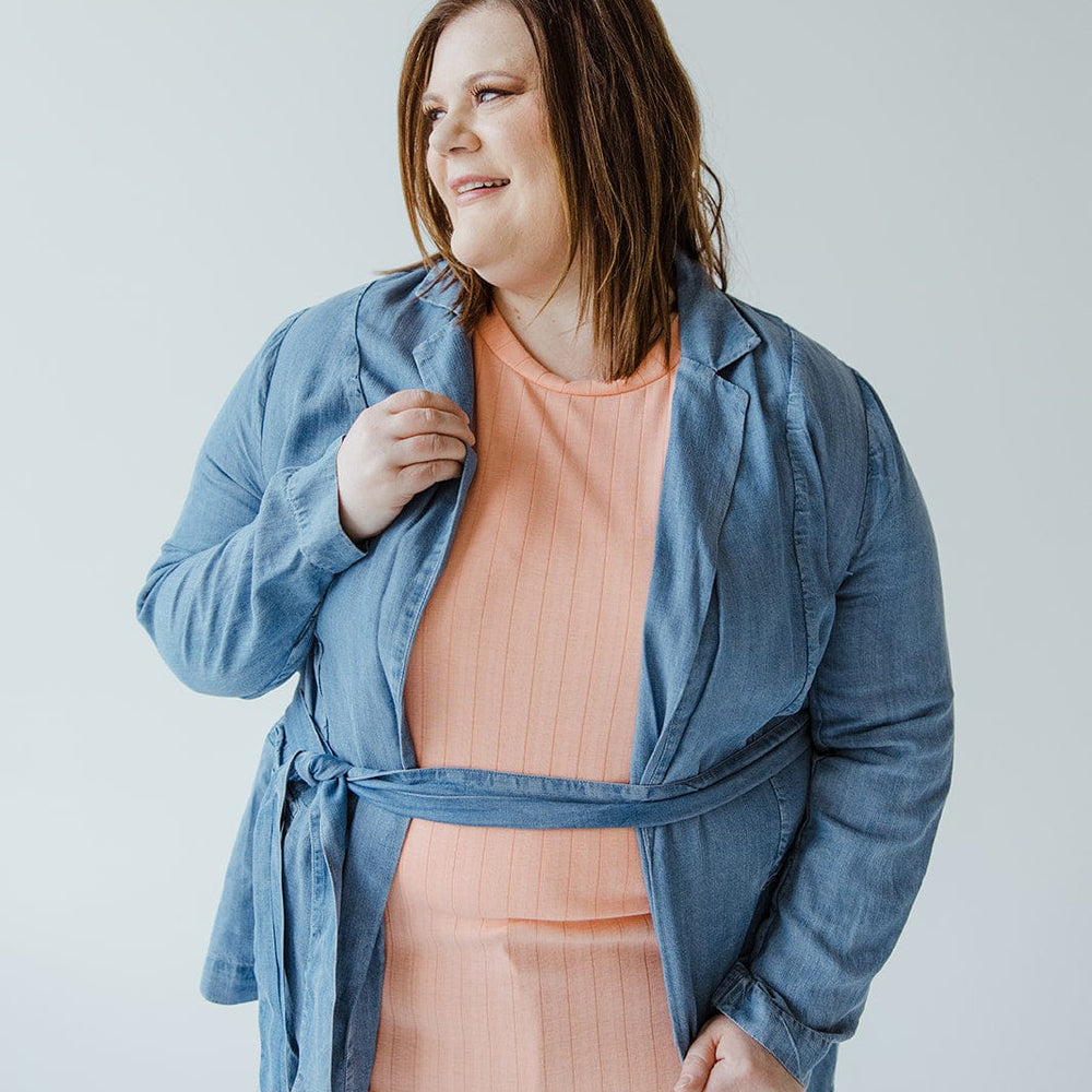 A person wearing a Dex CHAMBRAY BOYFRIEND BLAZER, featuring a notched lapel, along with a light orange shirt smiles against a plain background.