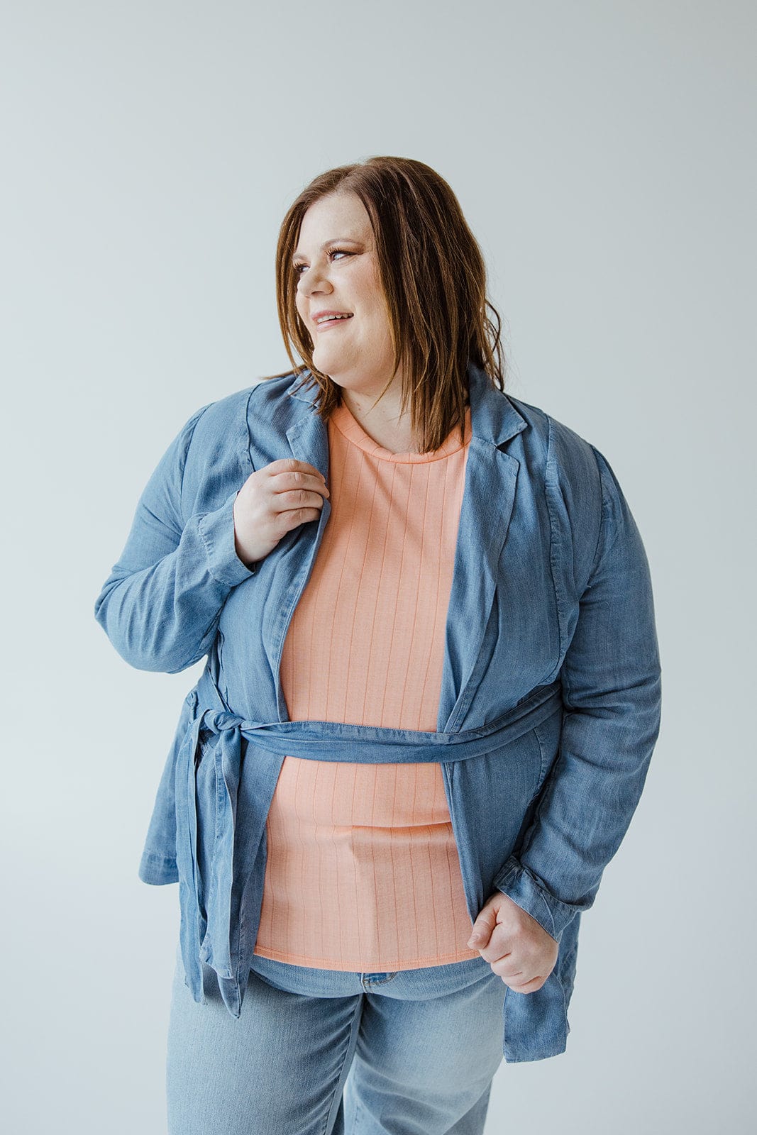 A person wearing a Dex CHAMBRAY BOYFRIEND BLAZER, featuring a notched lapel, along with a light orange shirt smiles against a plain background.