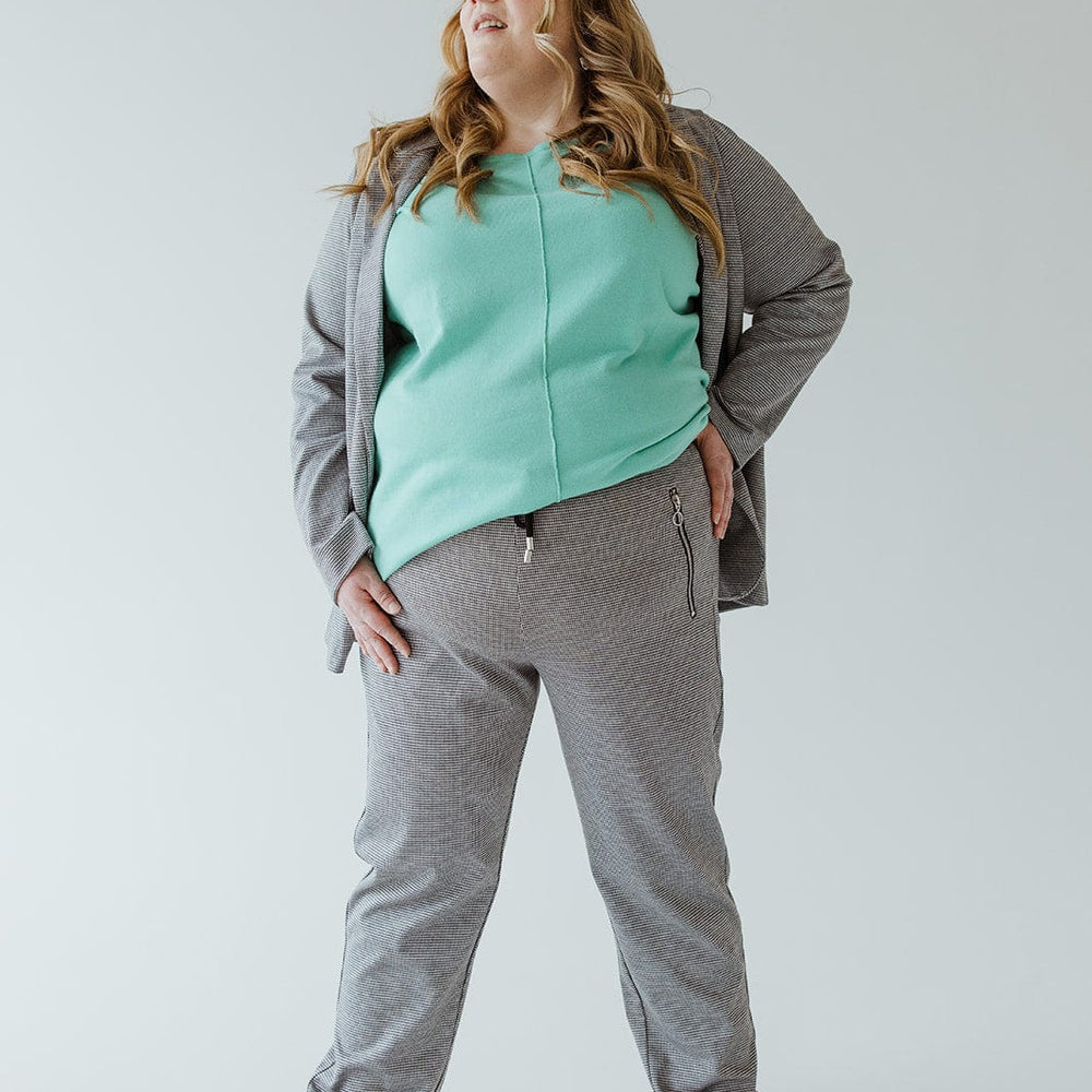 Person in gray tracksuit and mint green top stands with hands on hips, looking to the side, showcasing zipper detail pockets.