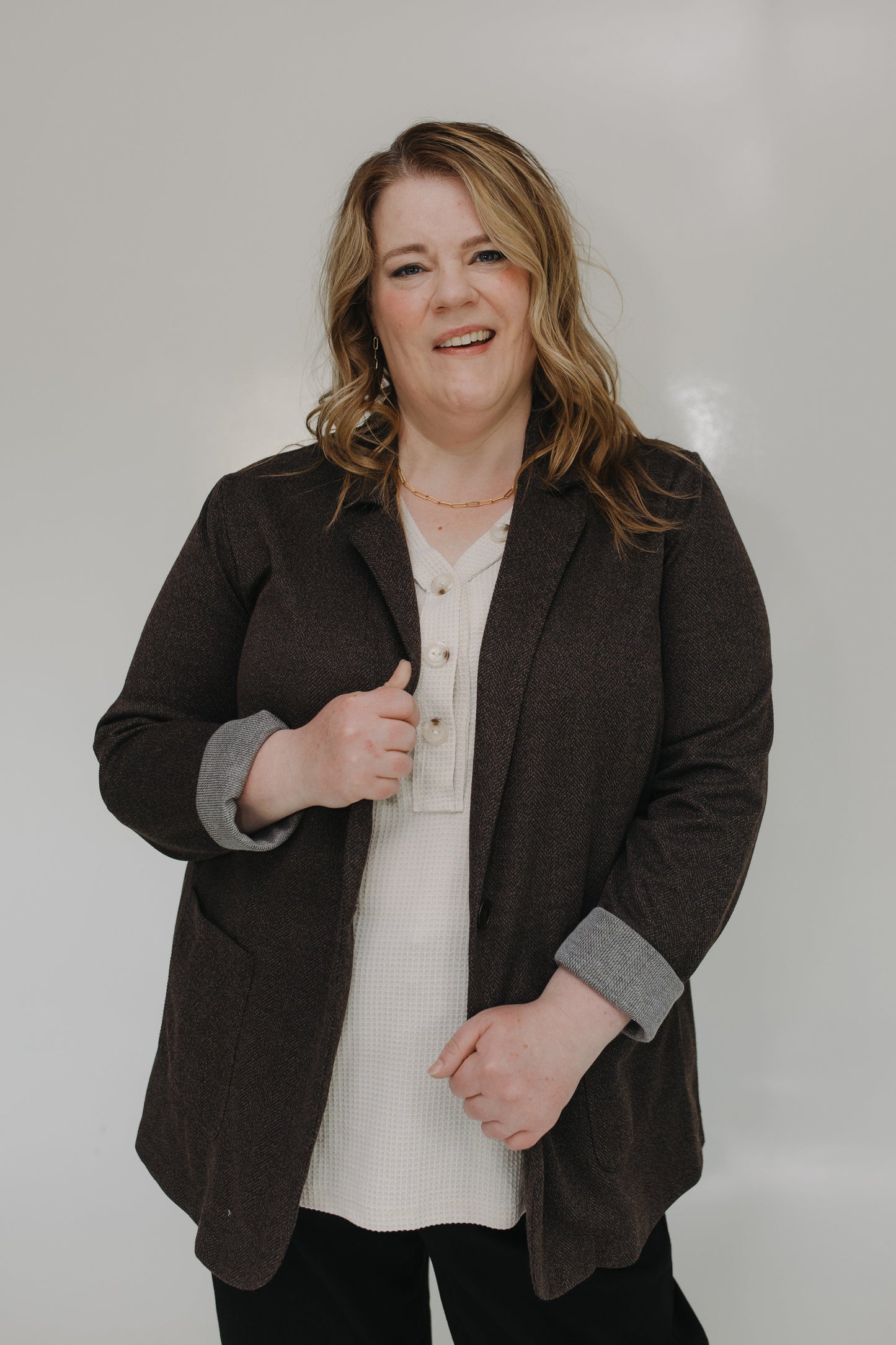 Woman wearing a brown blazer over a white shirt on a plain background