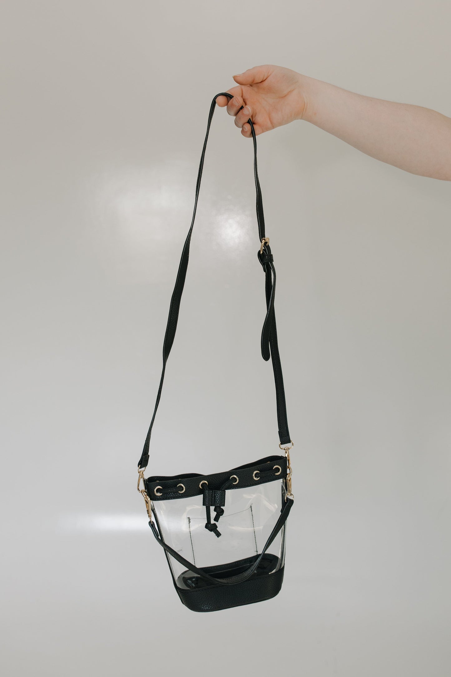 Black faux leather stadium bag held by a hand on a light gray background