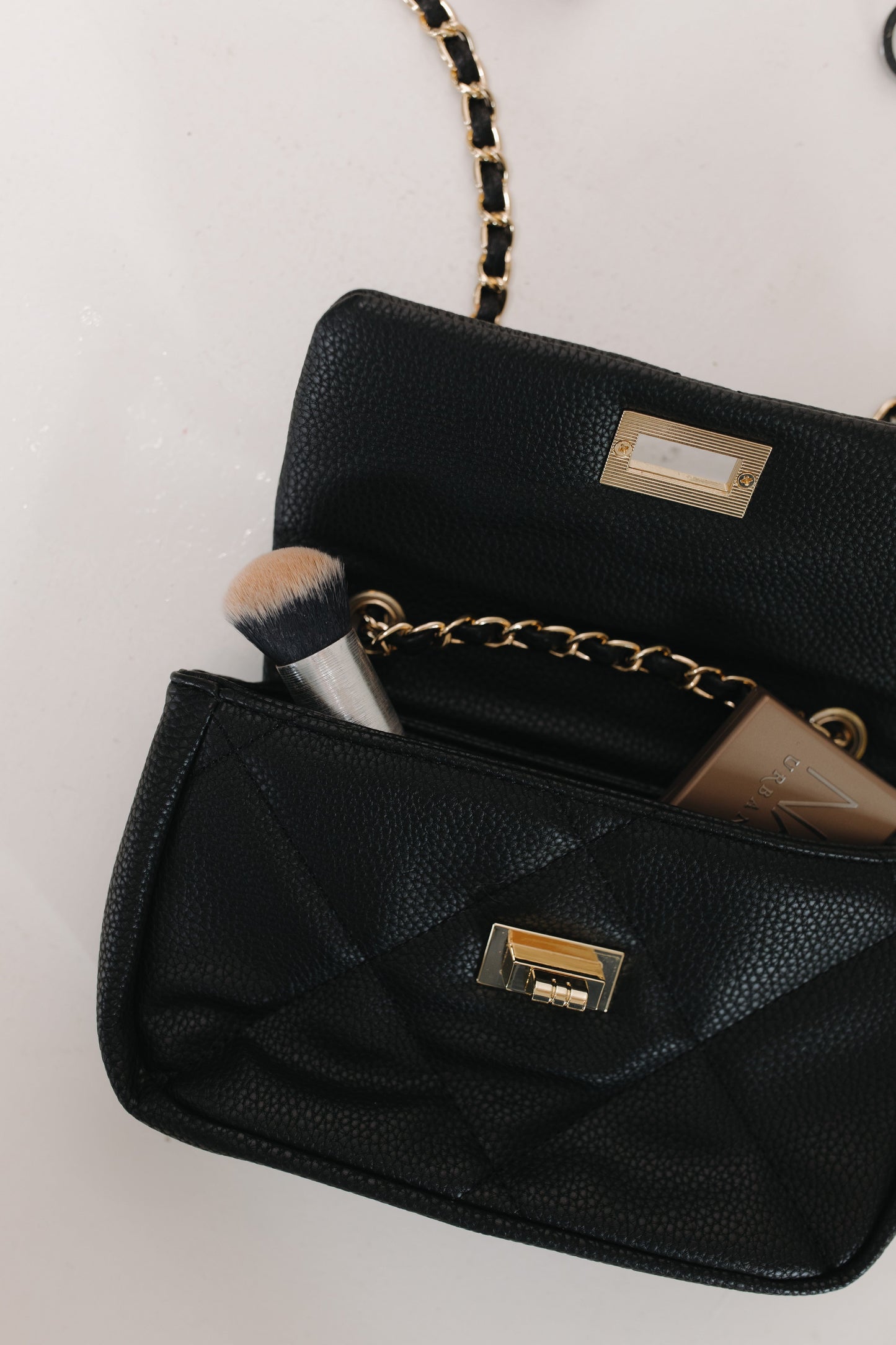 Black handbag with gold chain strap and clasp on a light background