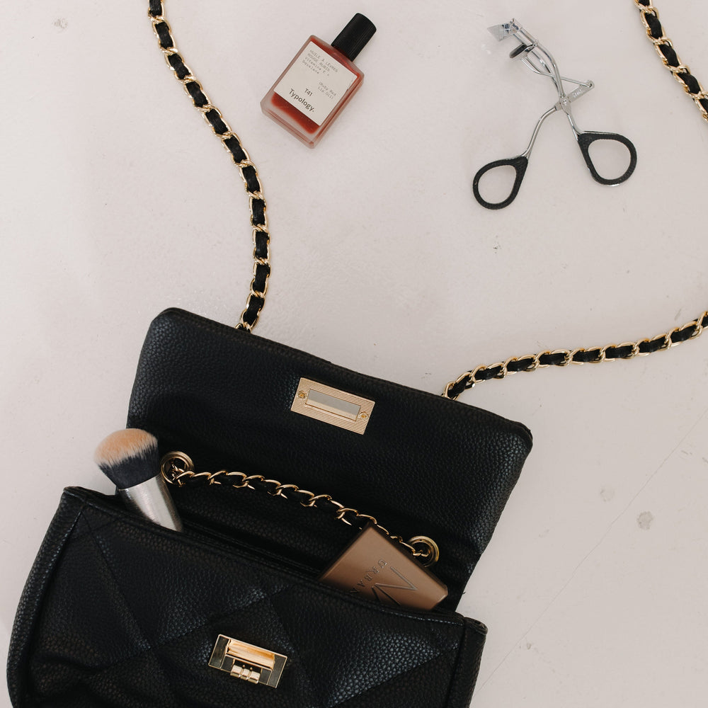 Black handbag with makeup items on a light background