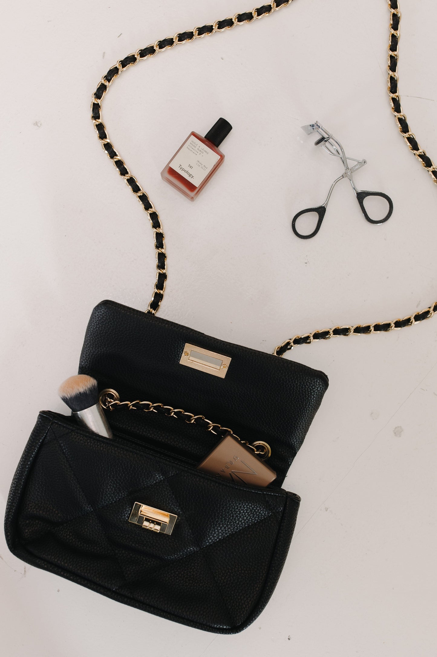 Black handbag with makeup items on a light background