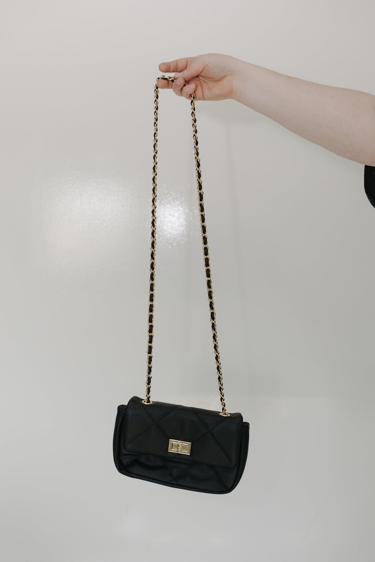 Black handbag with a chain strap held by a hand against a plain background