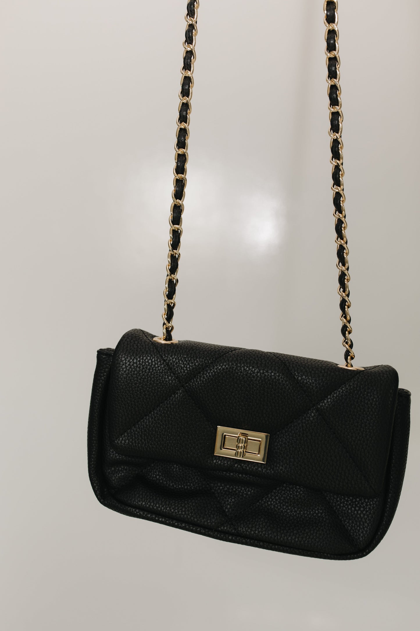 Black handbag with gold chain strap on a light gray background