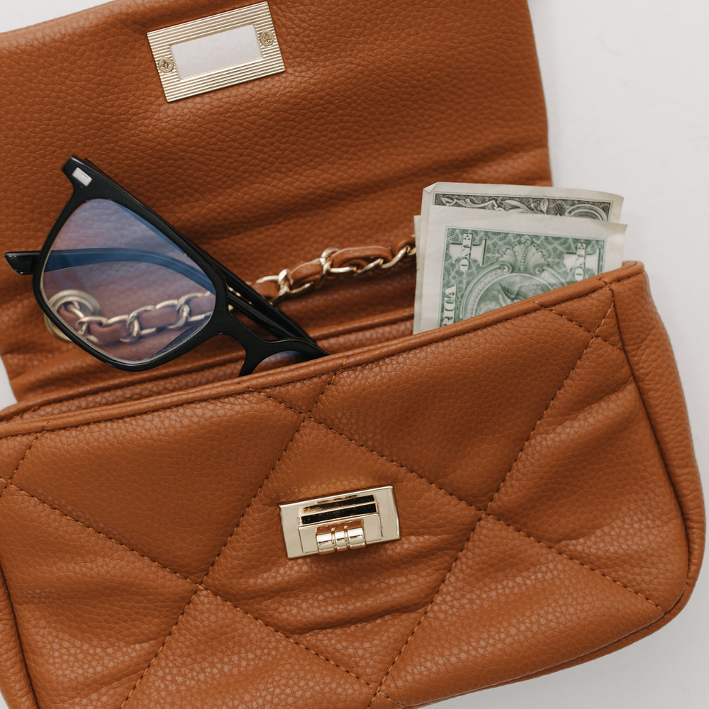 Brown quilted handbag with sunglasses and money on a light background