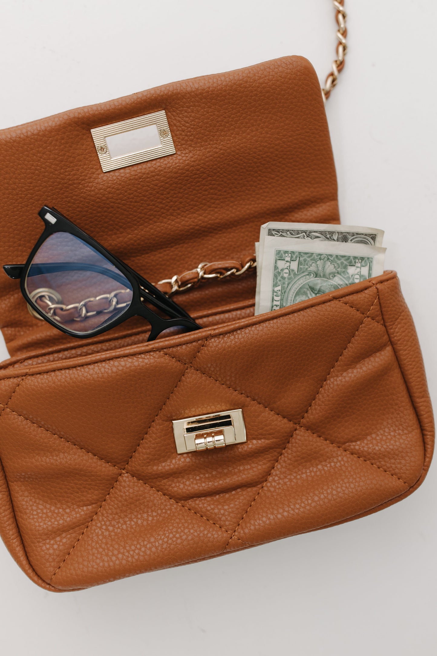 Brown quilted handbag with sunglasses and money on a light background